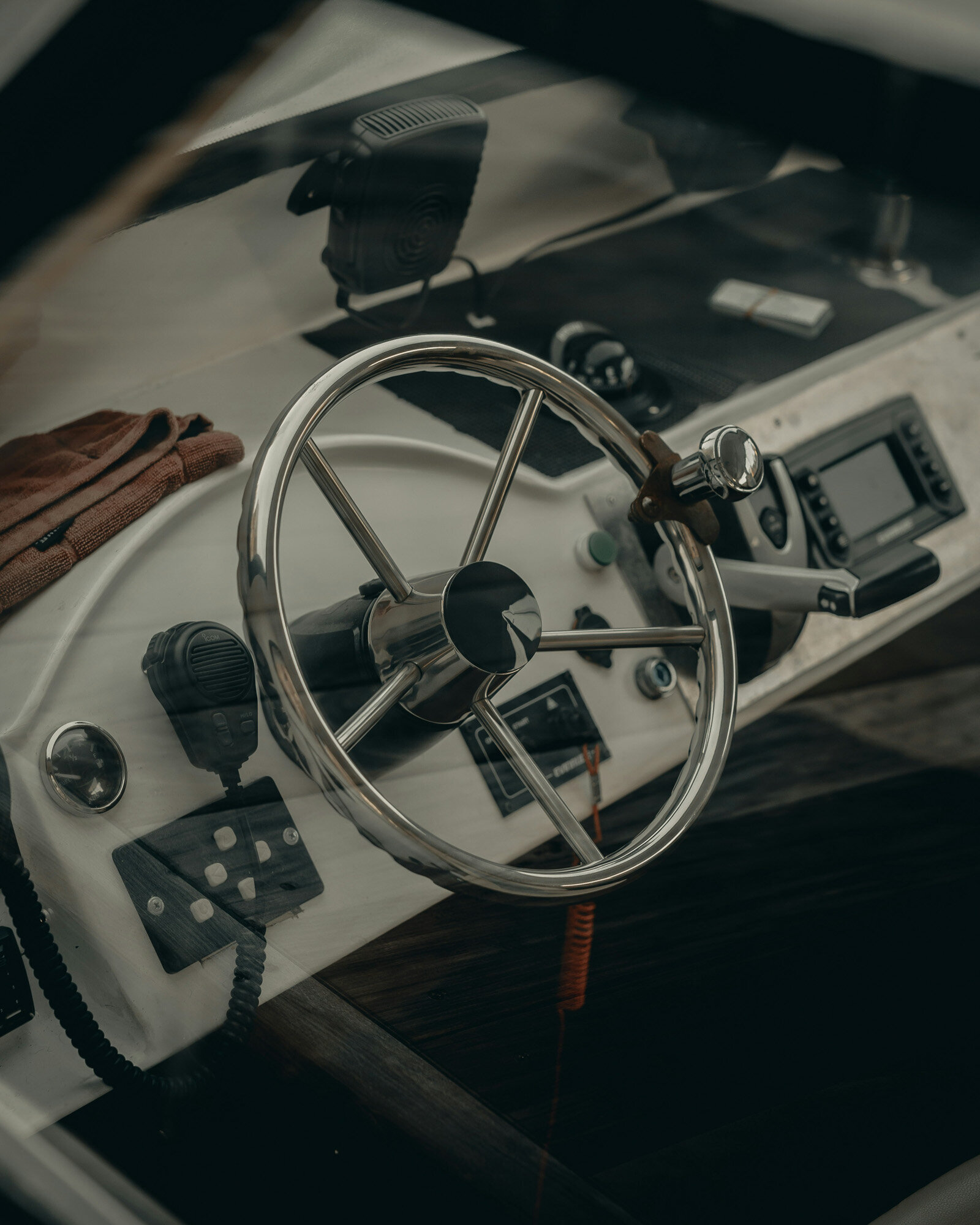 Close-up of a boat's cockpit, highlighting a shiny, silver steering wheel, a radio, a GPS display, and switche, a pair of gloves rests on the ledge near the windshield