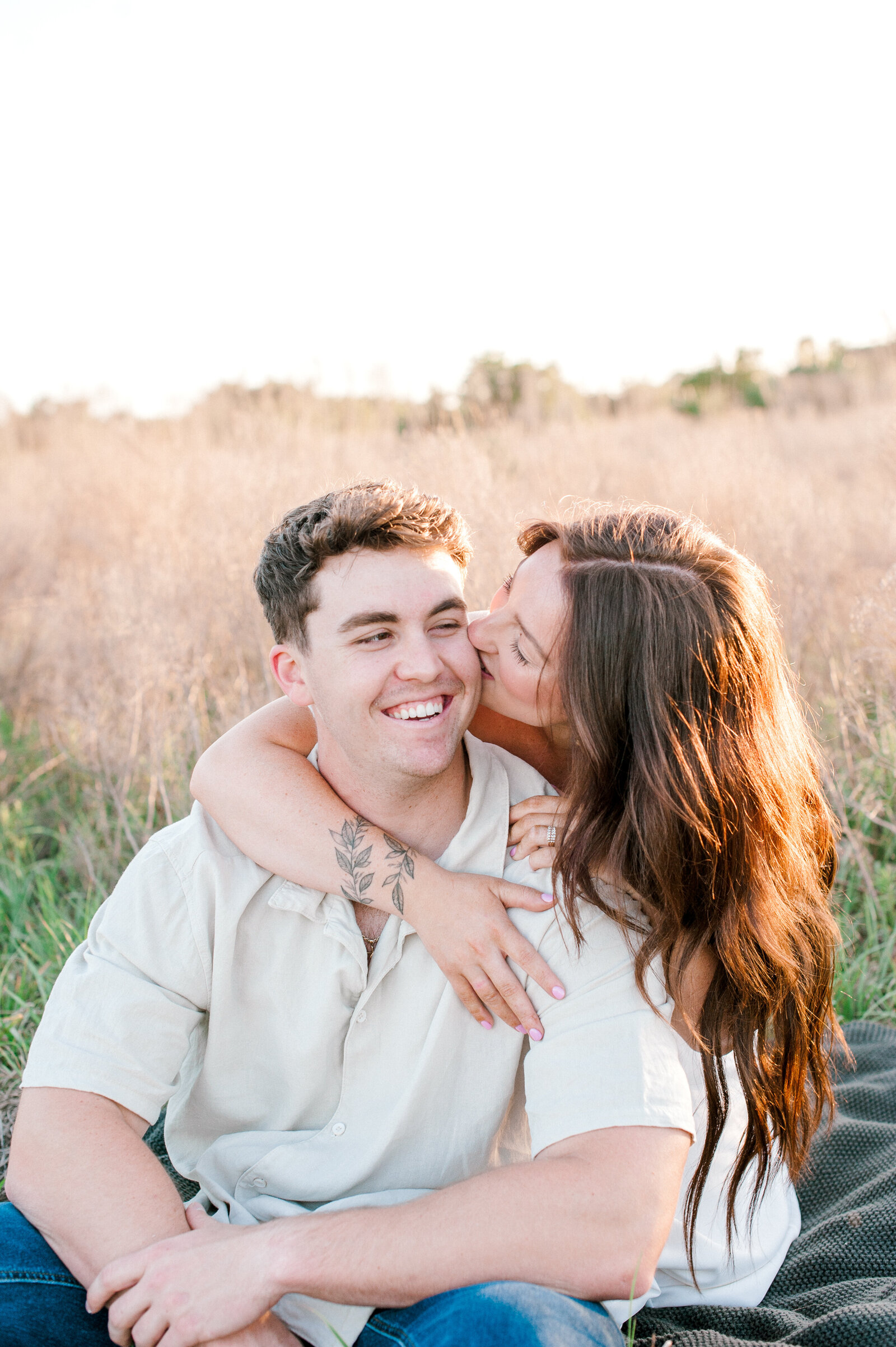 Girlfriend kissing her boyfriends cheek during their couples session in a tall grass field in Orlando