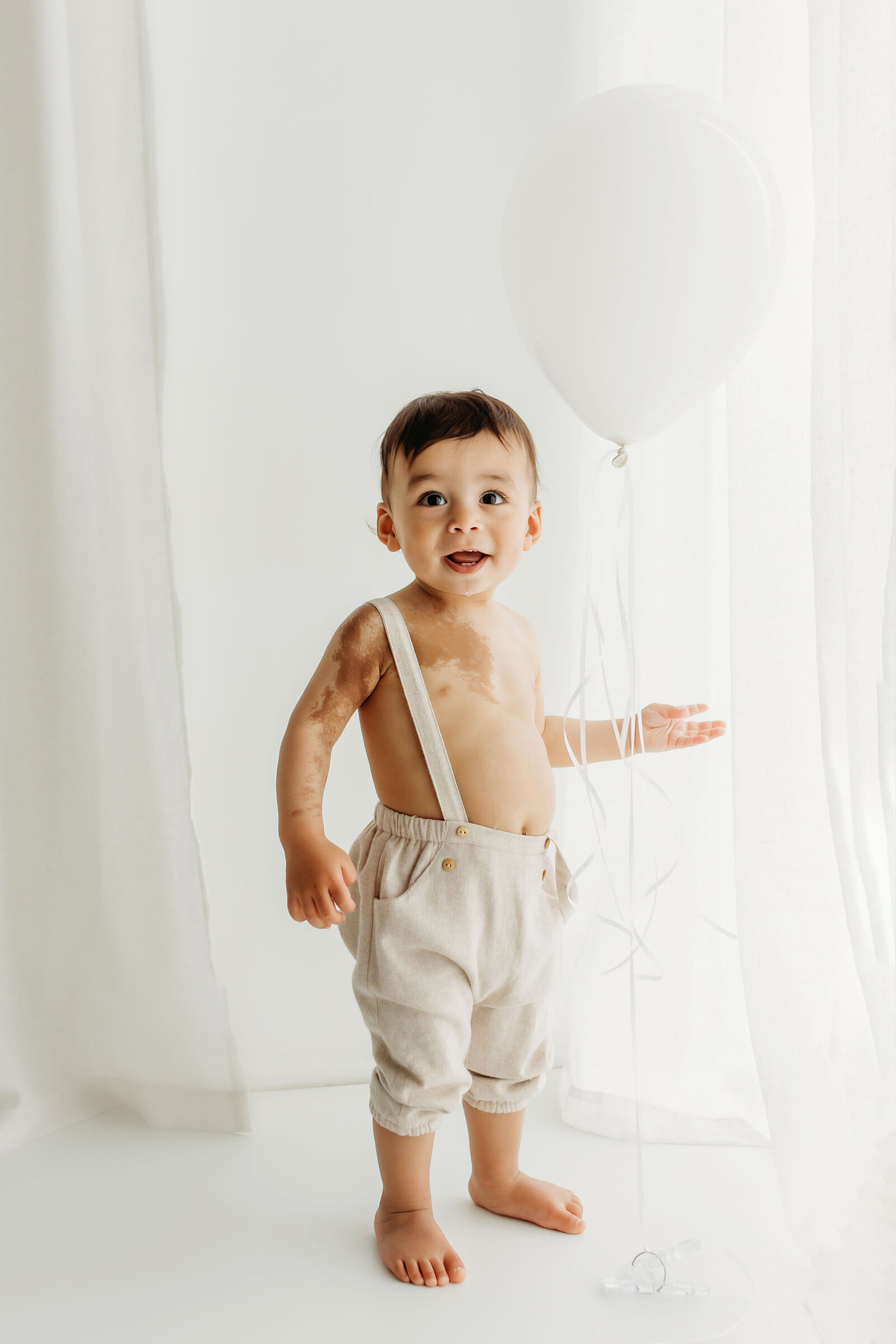 a one year old stands smiling at the camera inside a Vancouver Washington natural light photography studio