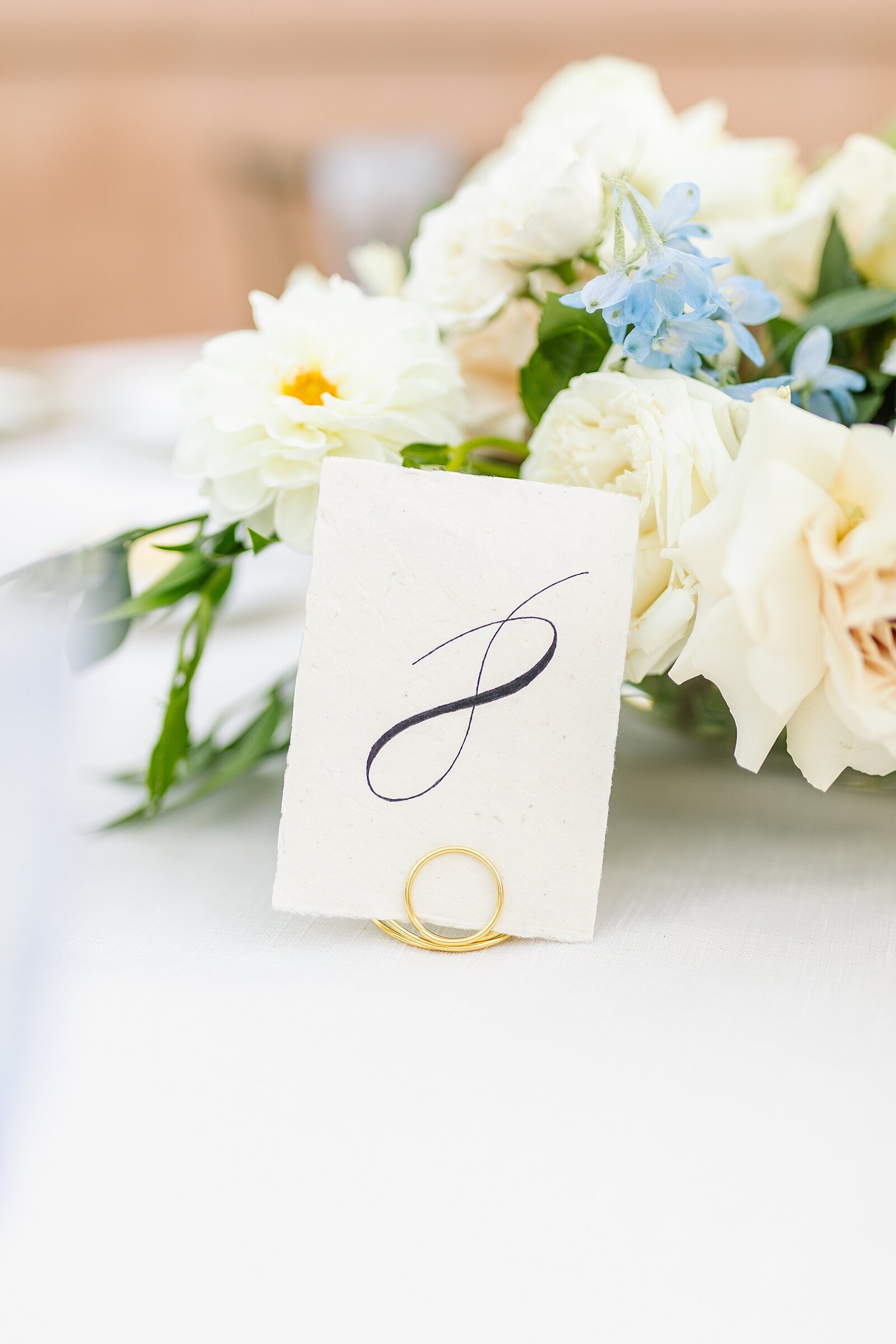 Wedding reception calligraphy  table numbers with gold stand in front of floral centerpiece at Rancho Valencia in Rancho Sante Fe.