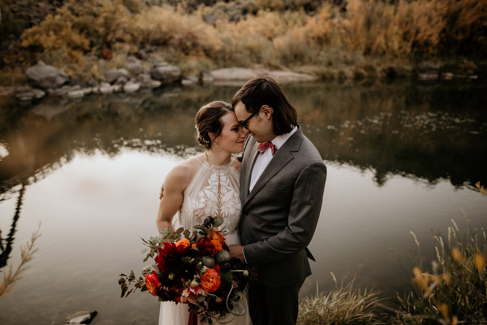 newlywed couple looking at each other in front of a river