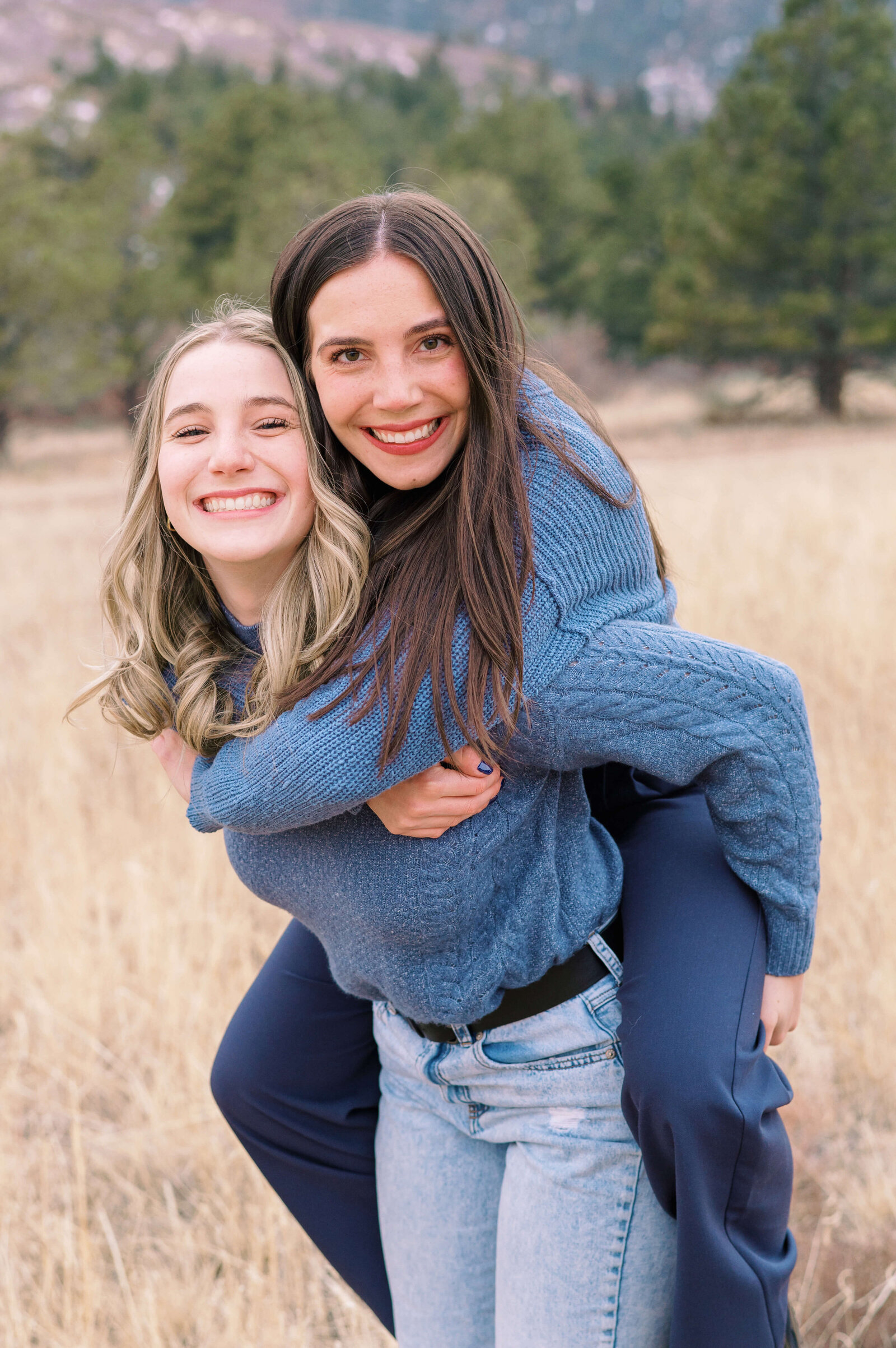 Northern Virginia family photographer takes a photo of one sister giving her older sister a piggy back ride and smiling at the camera