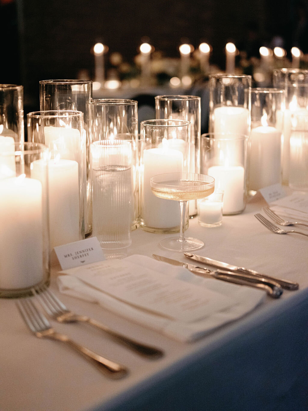 Candlelit reception table with ivory pillar candle centerpiece and ribbed glassware.