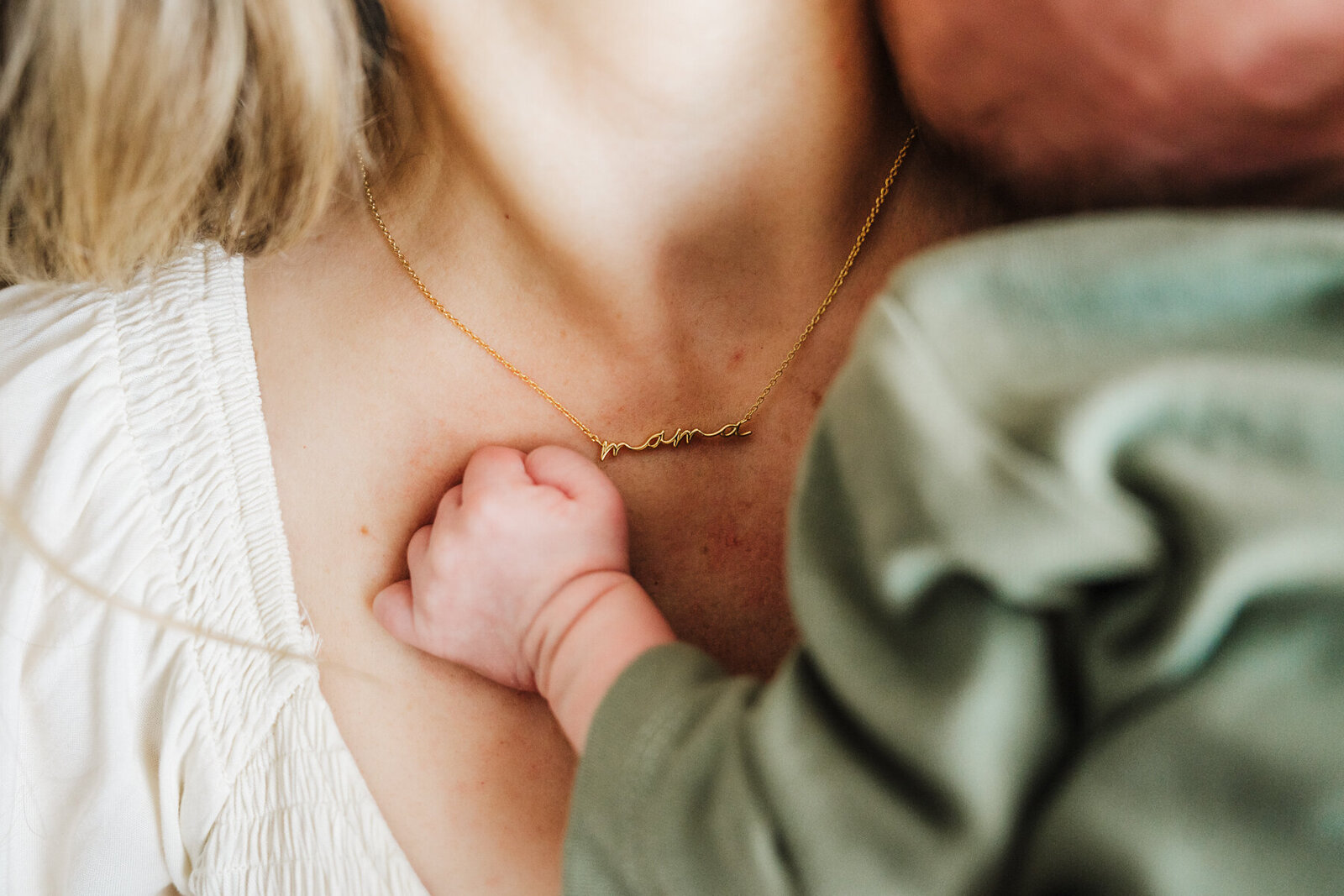close up of a mother wearing a mama necklace with newborn baby fist next to it