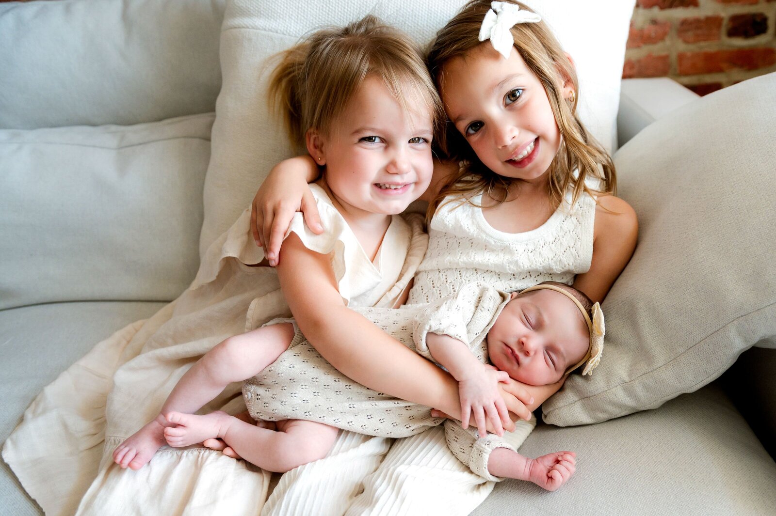 two girls dresssed in white dresses holding baby sister
