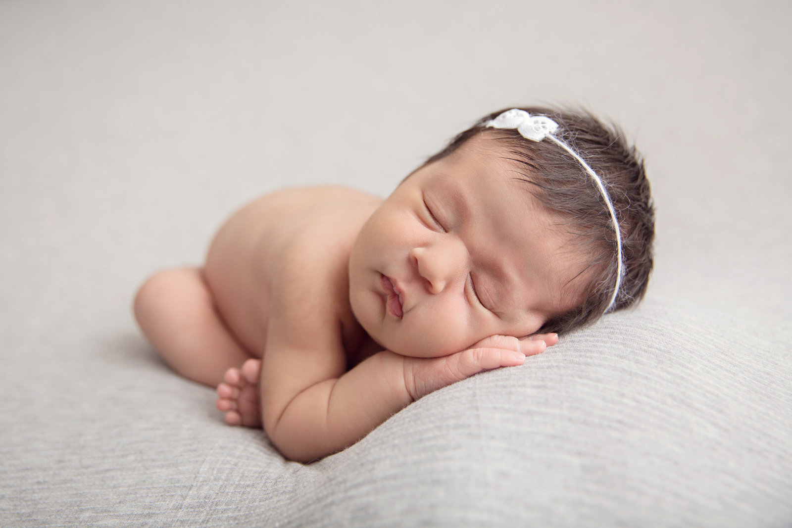 sleeping newborn baby in womb pose on light grey fabric with white bow tieback