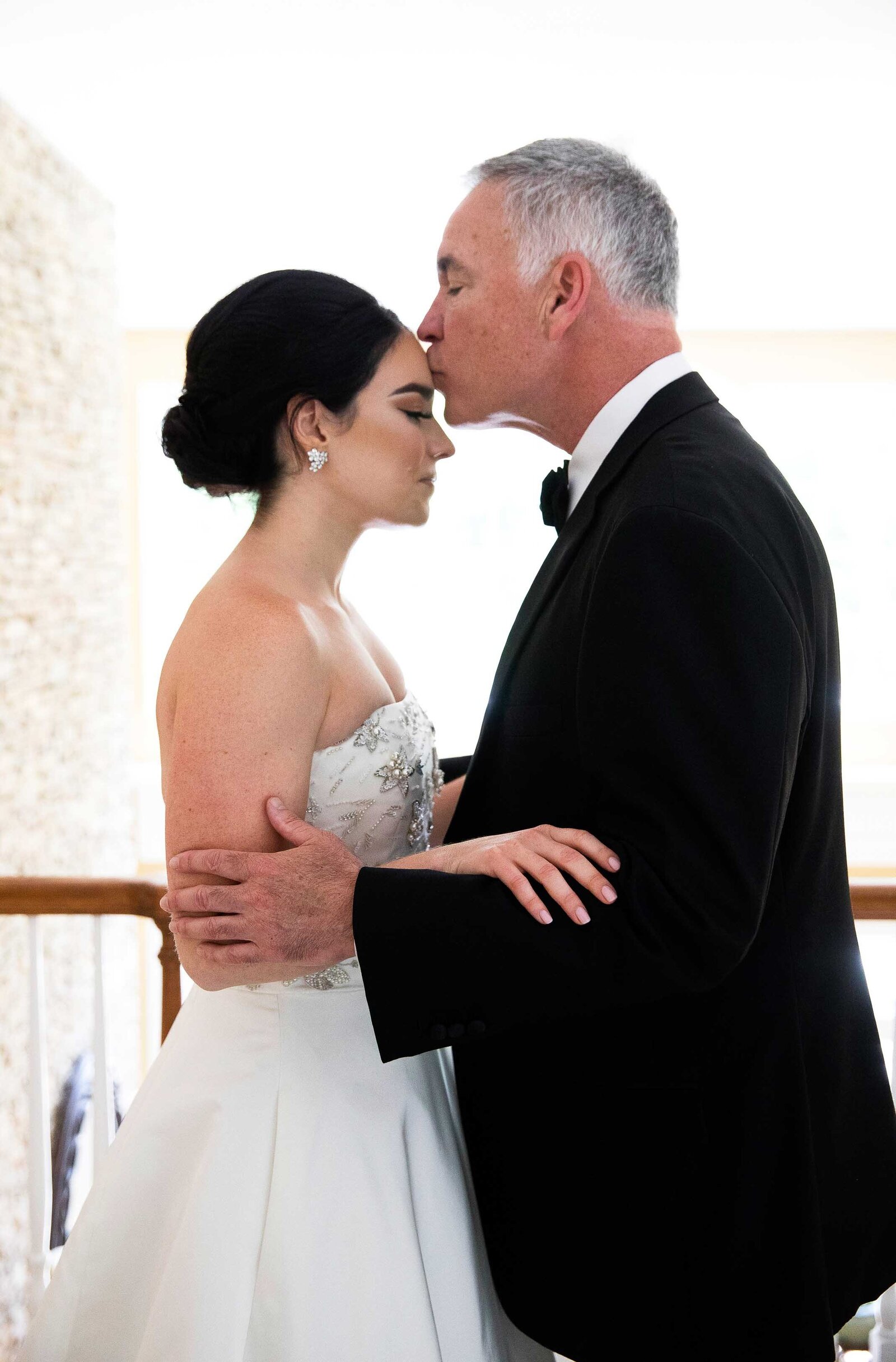 father of the bride embracing the bride, and giving her a kiss on the forehead