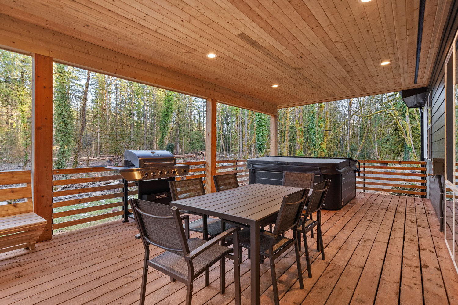 Outdoor dining area on a wooden deck with grill and hot tub