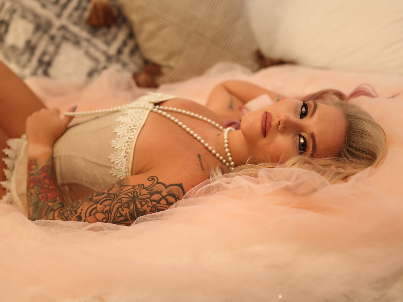 Boudoir portrait of blond woman laying in pink tulle with pink bustier and white pearls