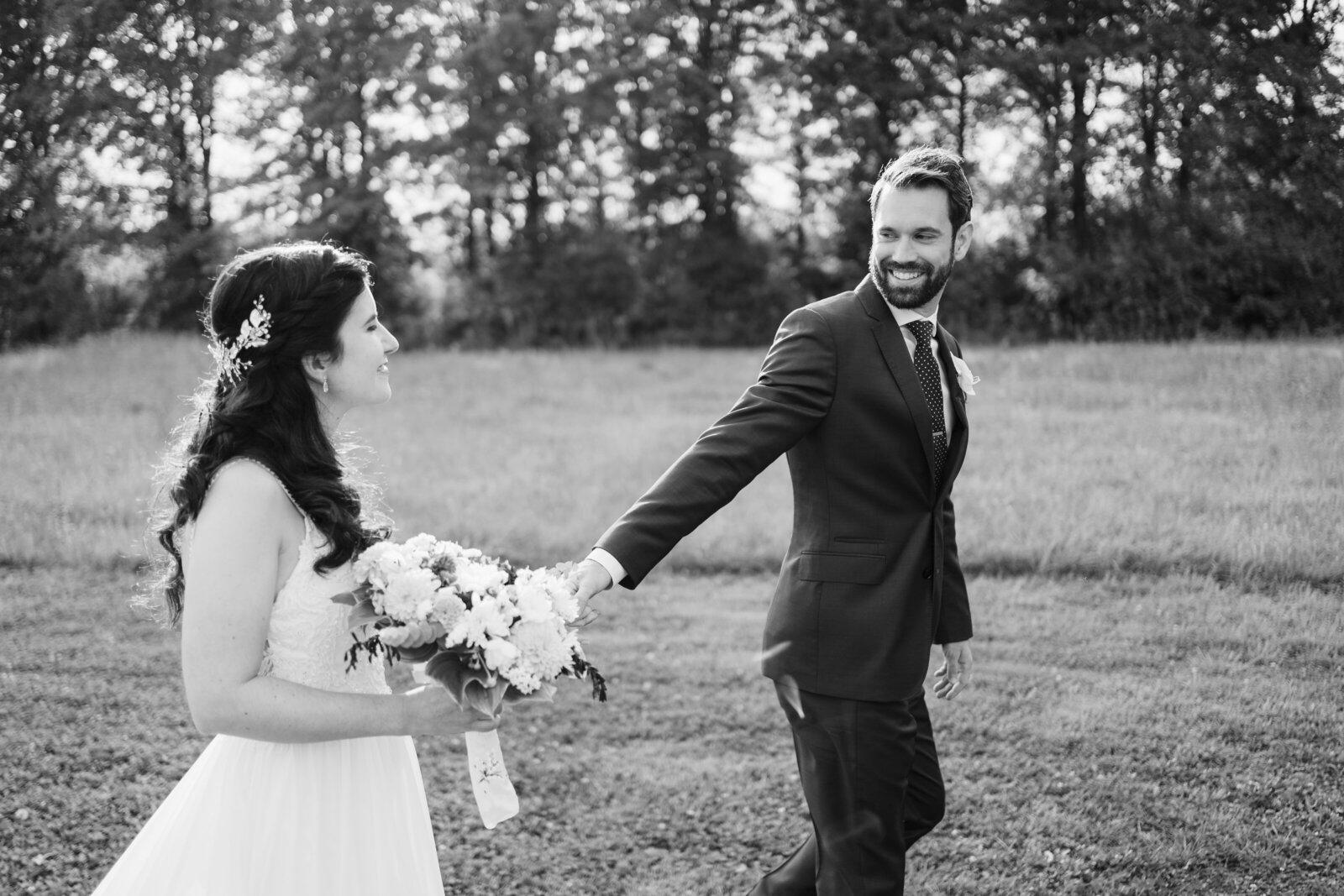 A groom holds his wife's hand and leads her across a field