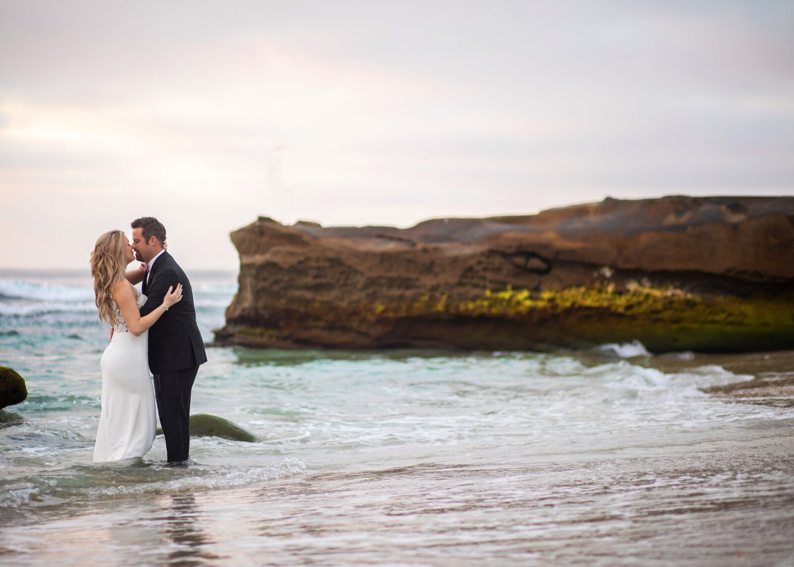 Adventurous destination wedding couple standing in the ocean in their wedding attire at La Jolla Beach, California for destination elopement.