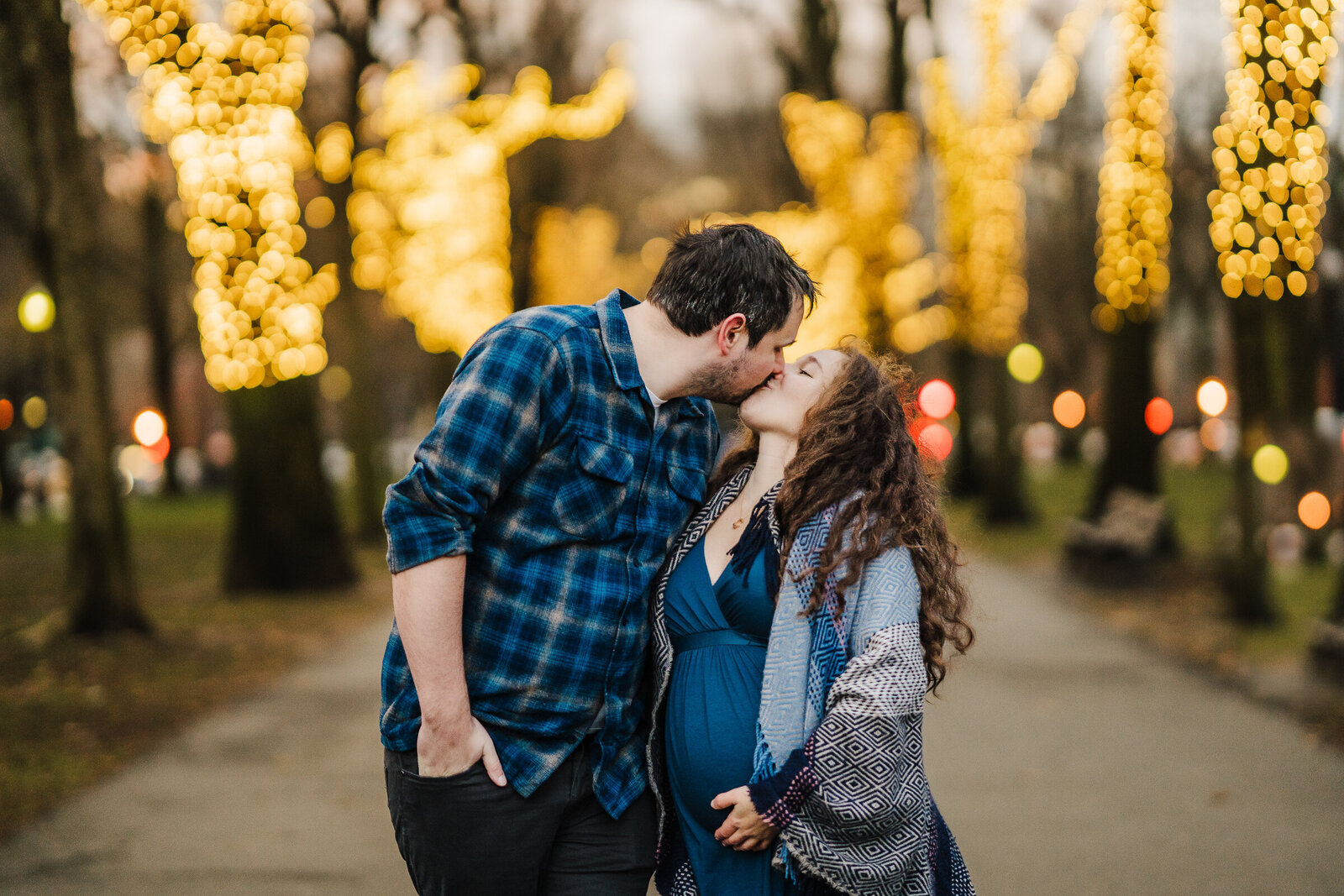 pregnant couple kisses by holiday lights
