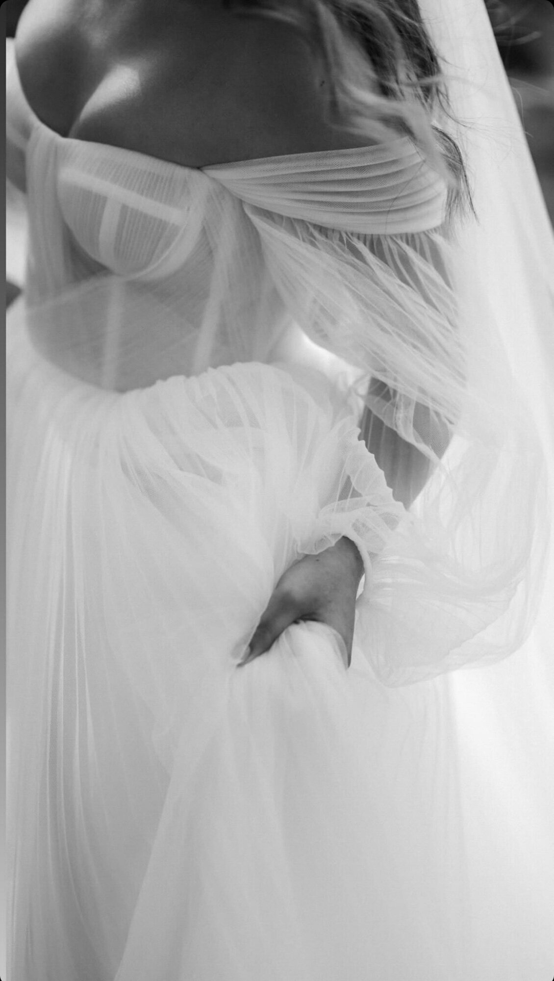 A close-up, black-and-white photo of a bride in an off-the-shoulder wedding gown with sheer fabric and intricate detailing altered by Bridal Alterations by Kirstyn, a Long Island seamstress