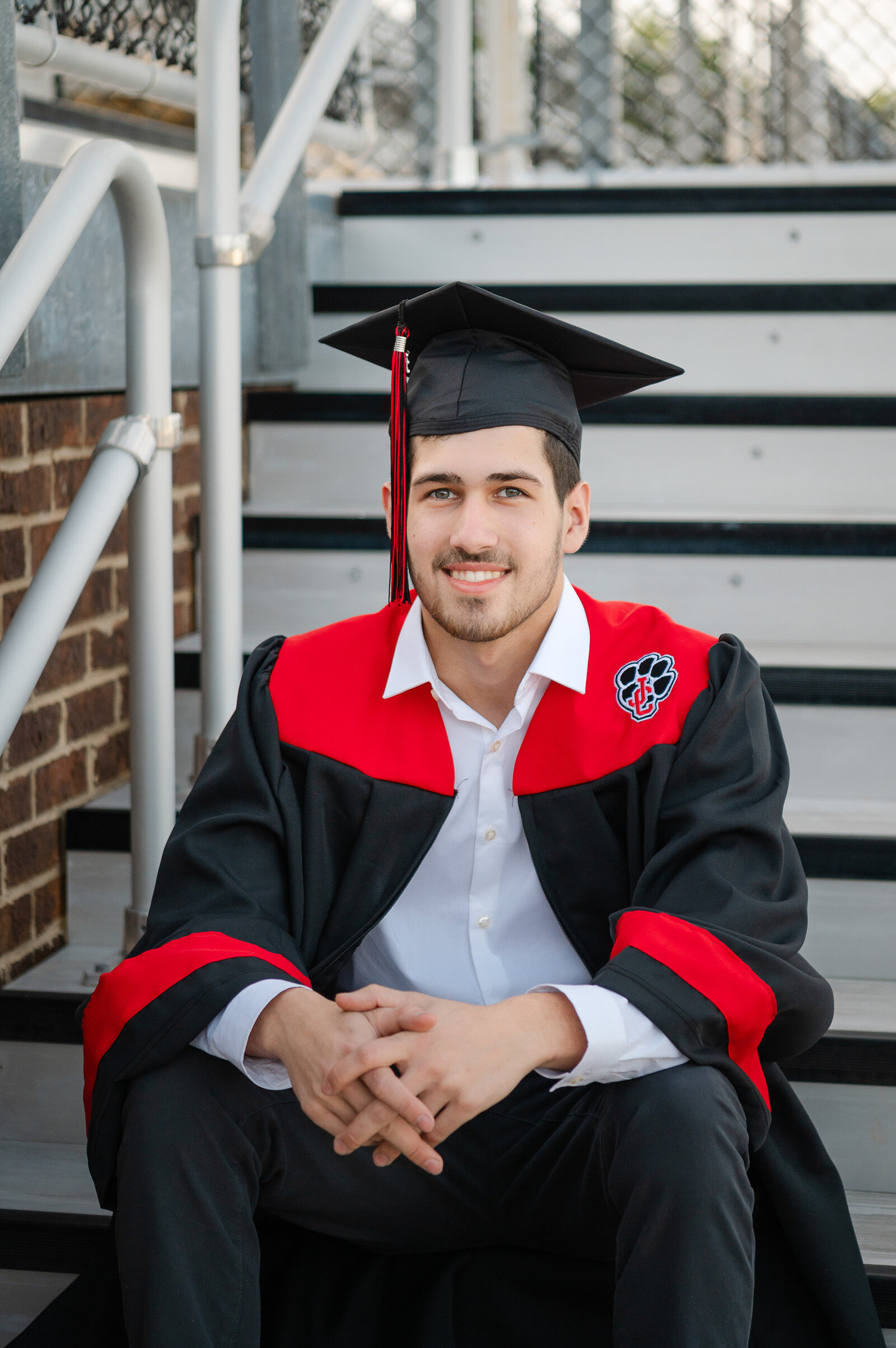 High school senior sits on the steps in the football stands while wearing his cap and gown