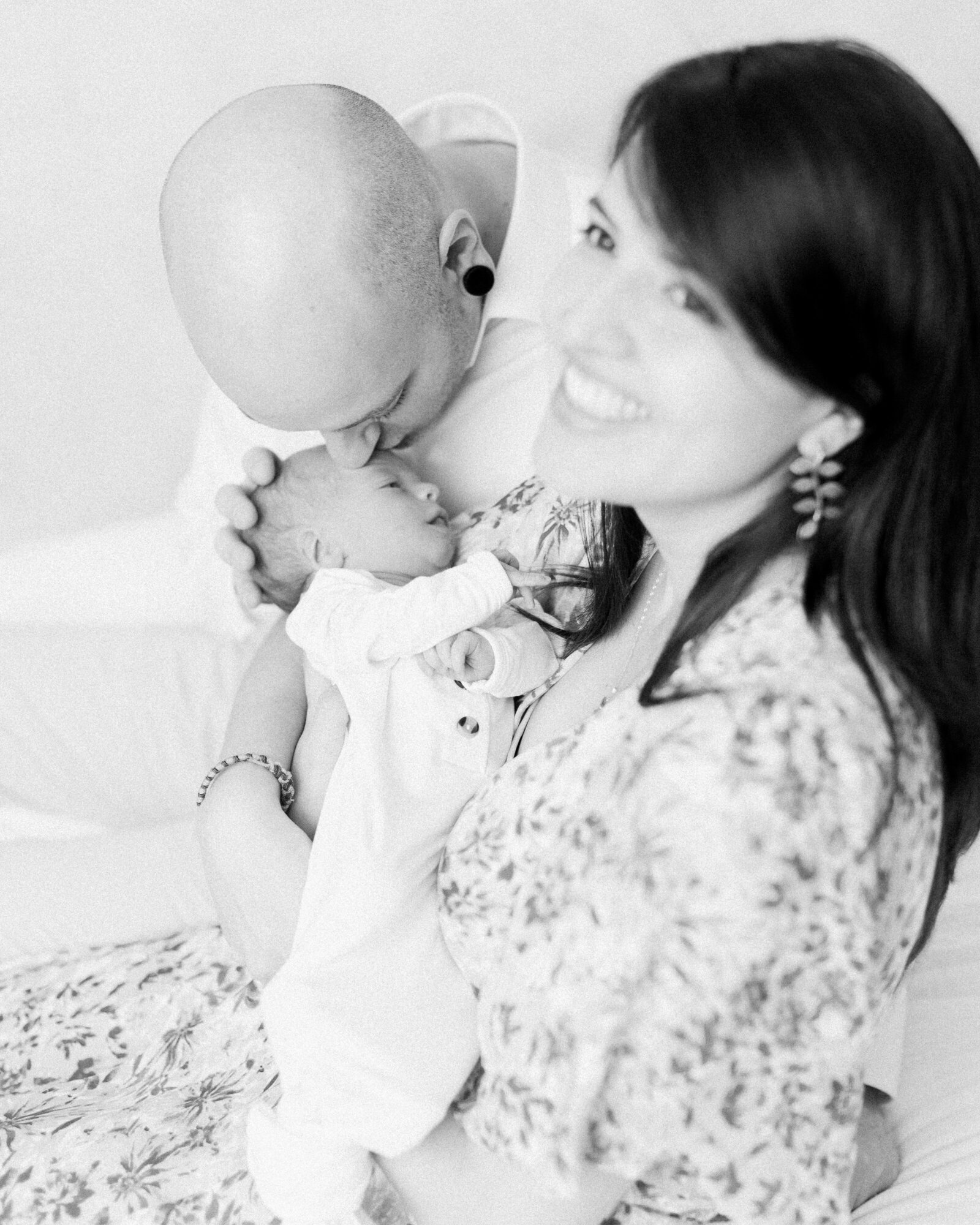 New mom cradling her baby while dad kneels over and kisses baby on the head by NH newborn photographer Fieldstone Studio.