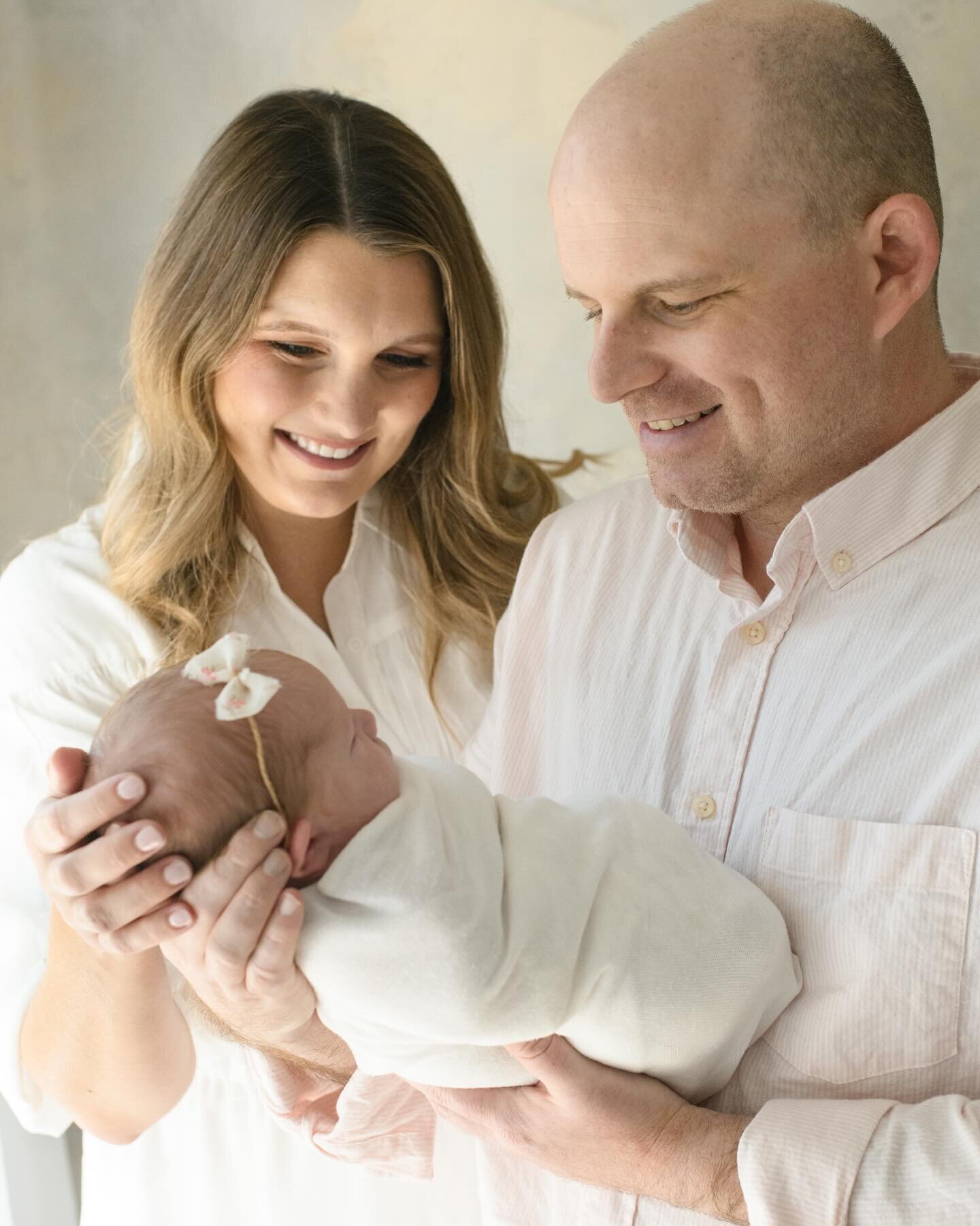 Dad cradles newborn wrapped in a blue ribbon as mom leans over with a smile. A soft in-home newborn session by Moments in Light Photography.