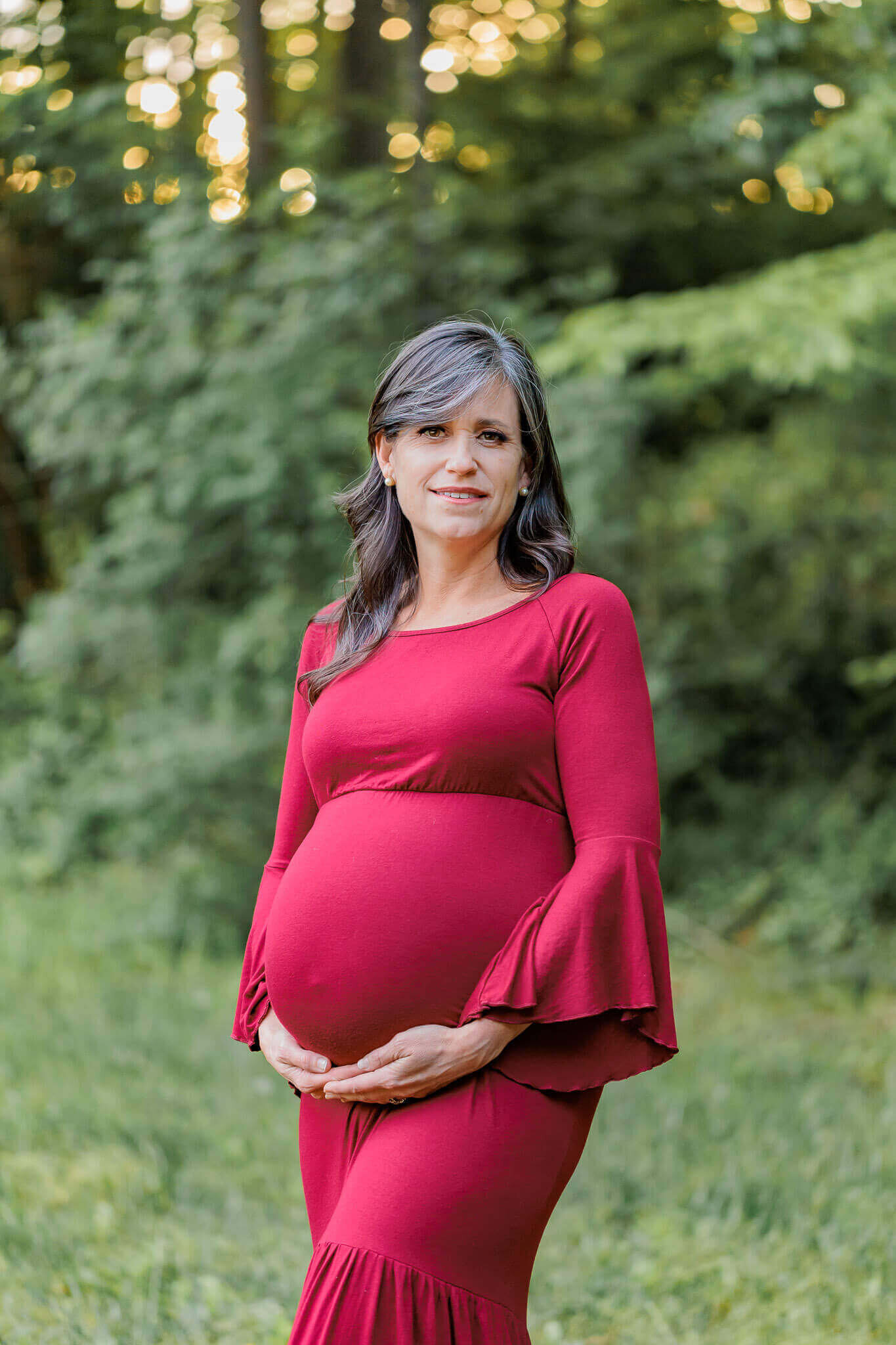 A beautiful mother-to-be in a red dress at a park in Burke.