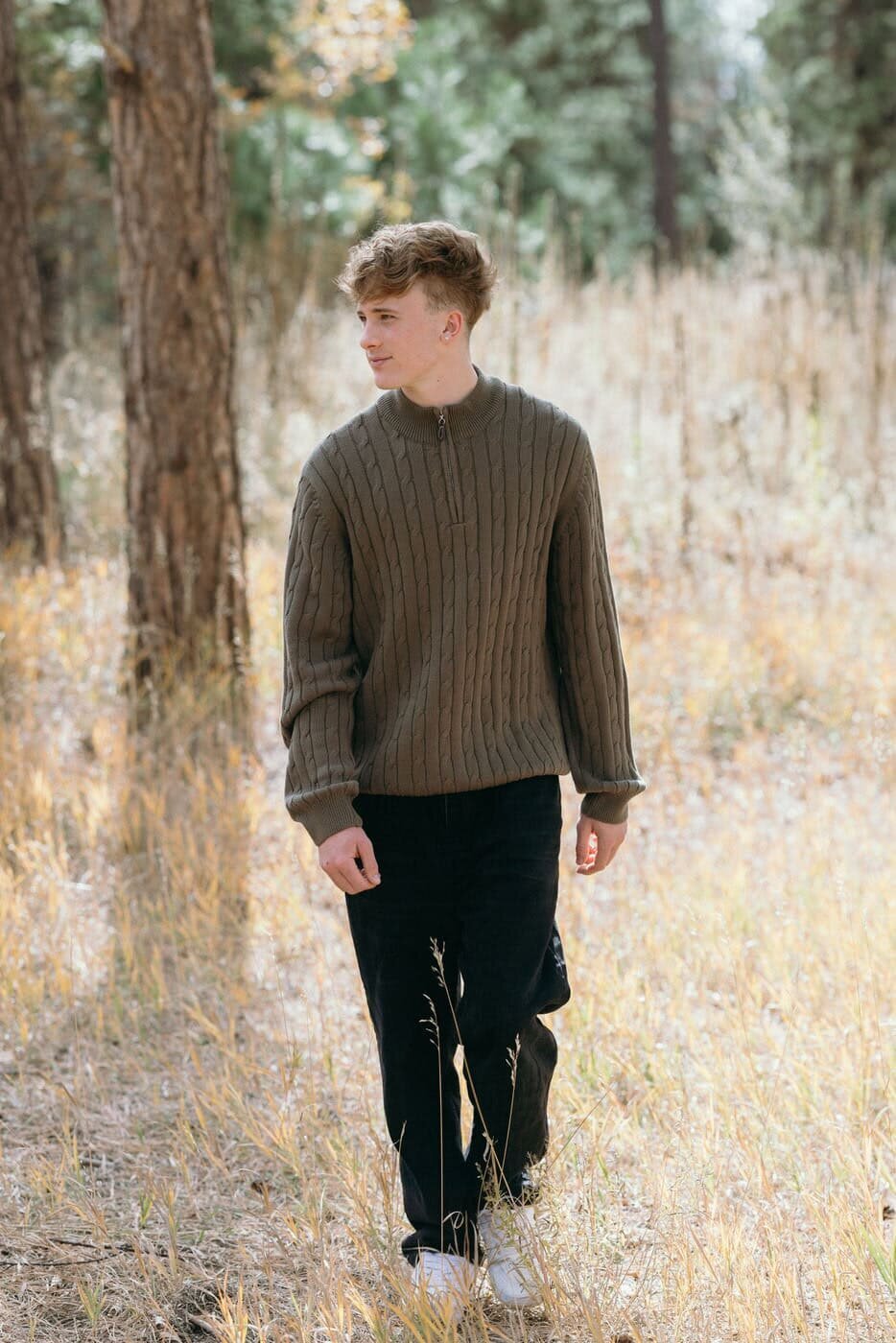 A high school senior looks off to the side as he walks towards the camera. 
