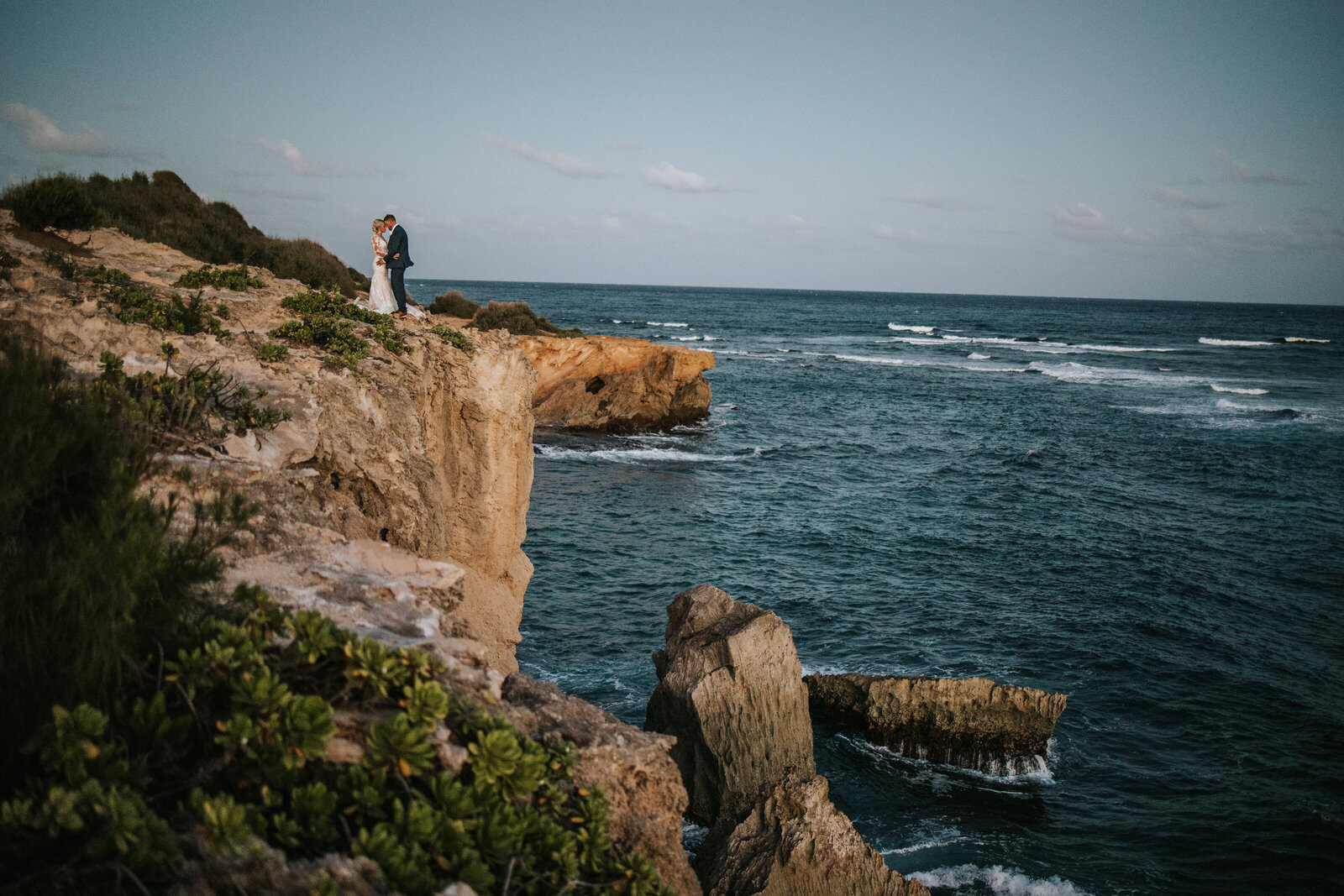 Beautiful couple standing on the cliff-side overlooking the ocean on their elopement wedding day.