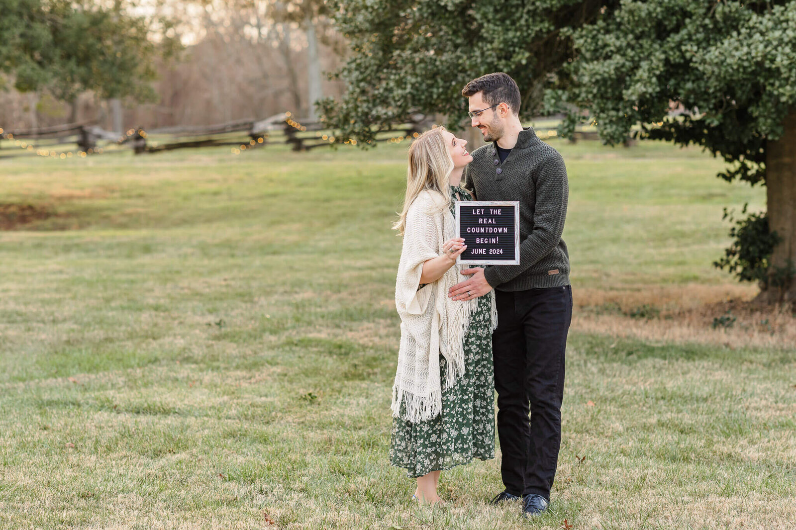 A couple expecting a baby embracing each other and holding a sign announcing their baby.