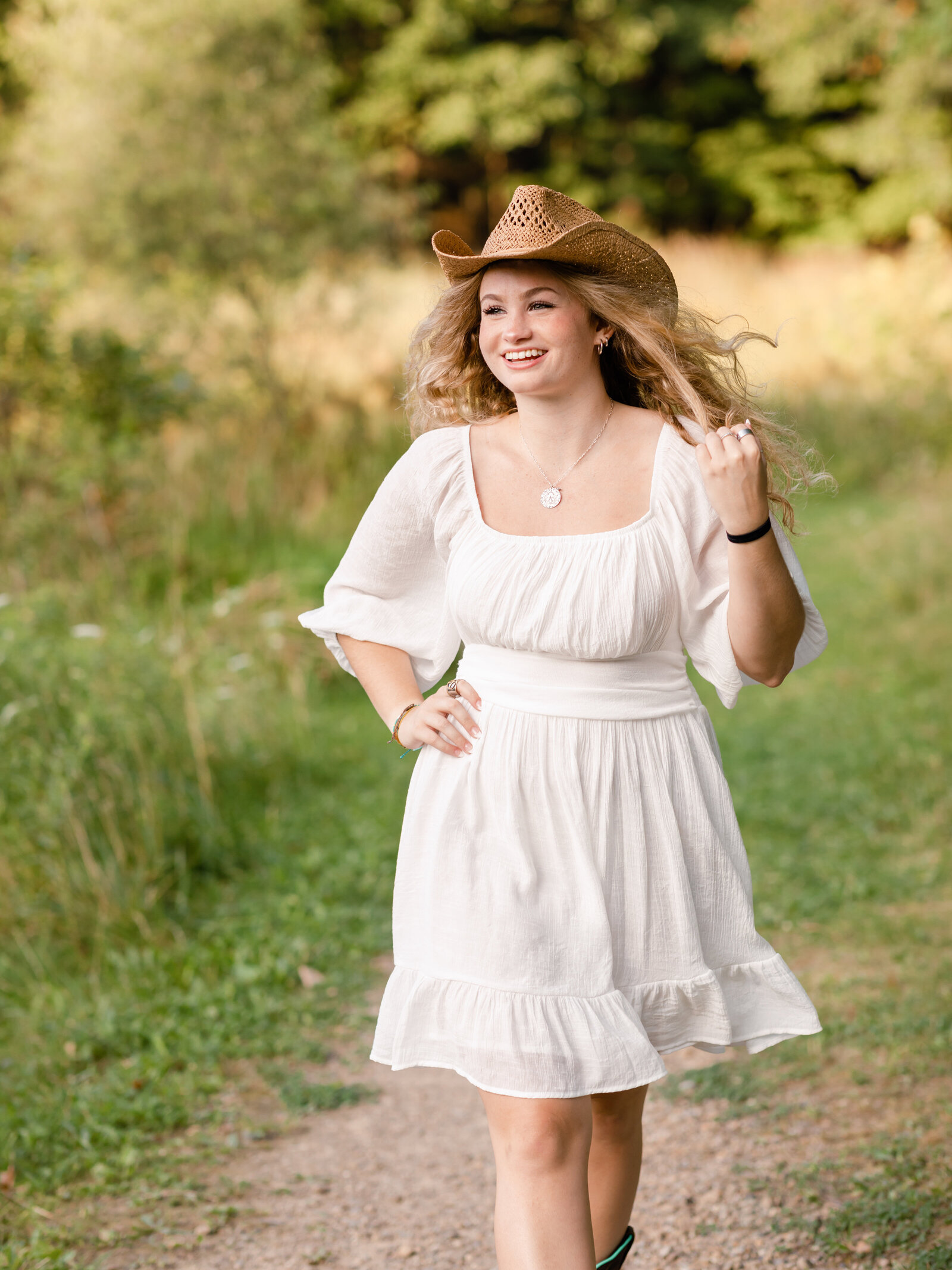 girl with cowboy hat and white dress walking in park for senior photos