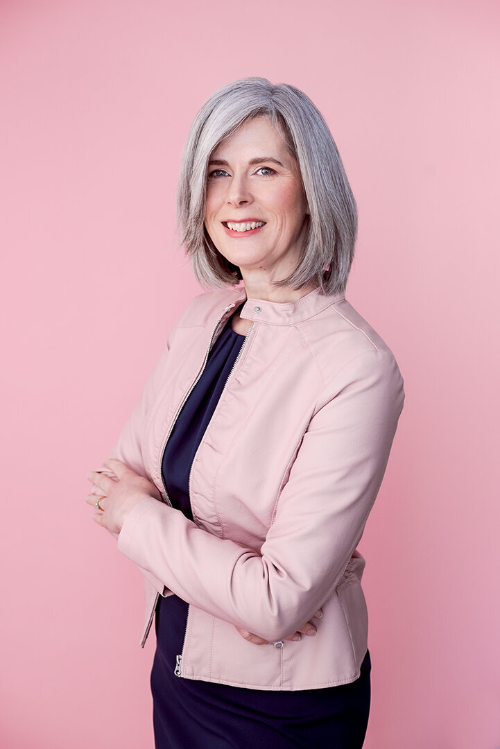 Headshot of a dietician with grey hair wearing a smart pink moto jacket