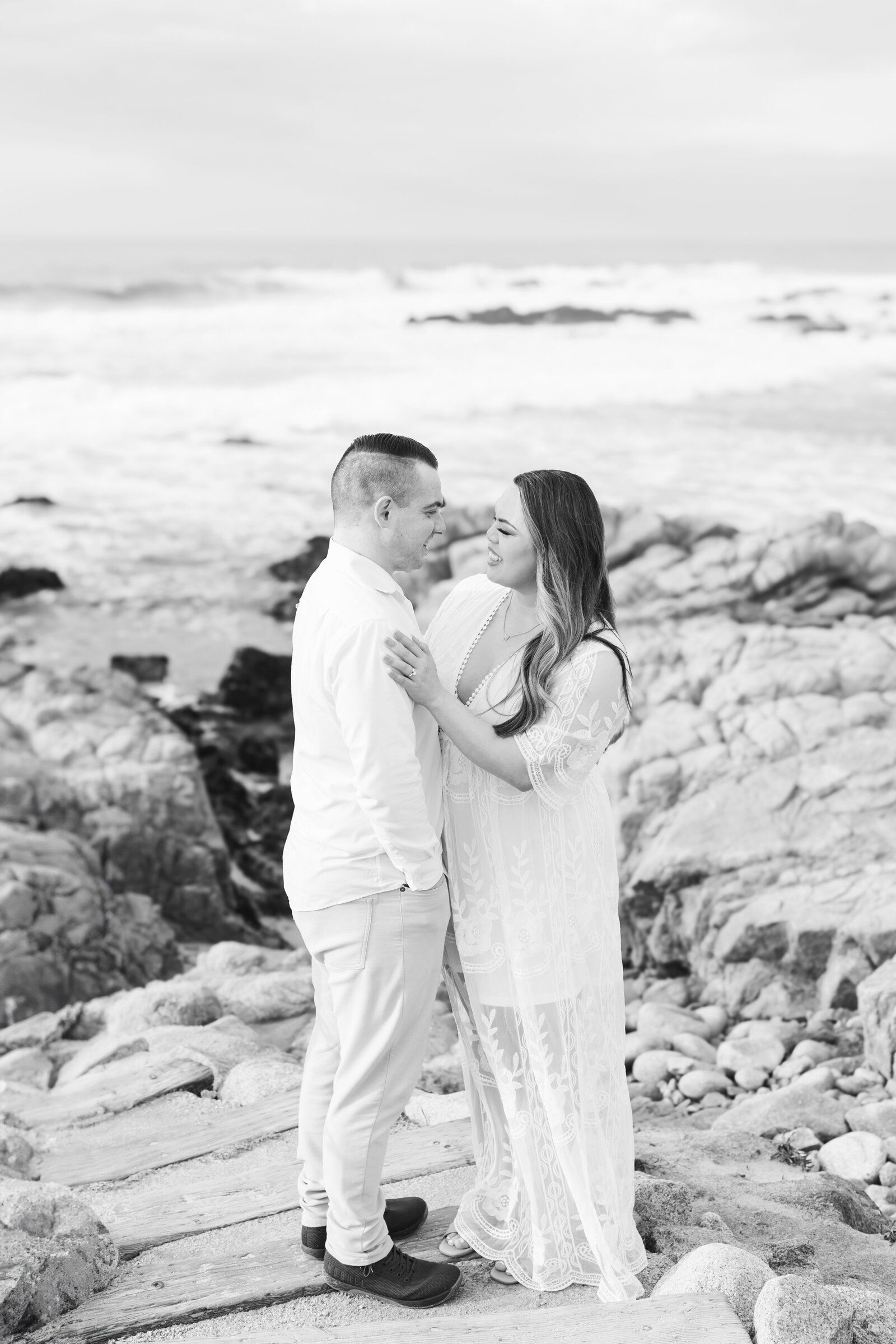 An engaged man and woman take photos on the beach in Pacific Grove, Monterey, California near Big Sur.
