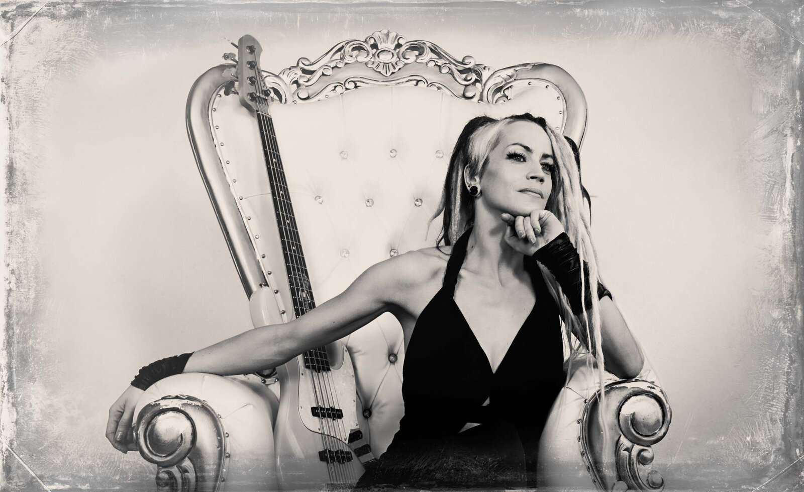 Music portrait Tanya O Callaghan wearing black dress sitting with bass guitar beside in large white arm chair black and white