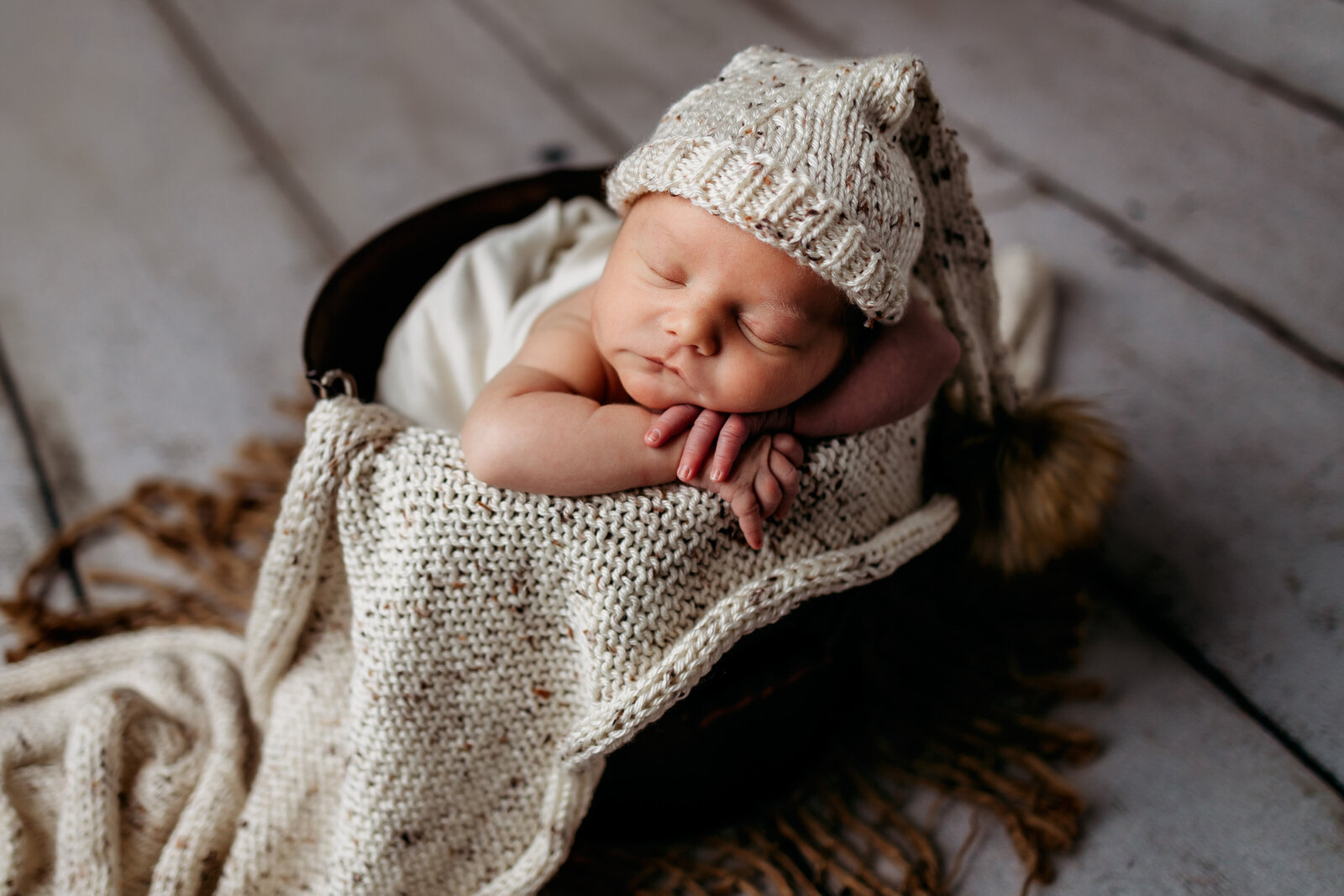 Newborn boy sleeping in bucket wearing a cream sleepy cap