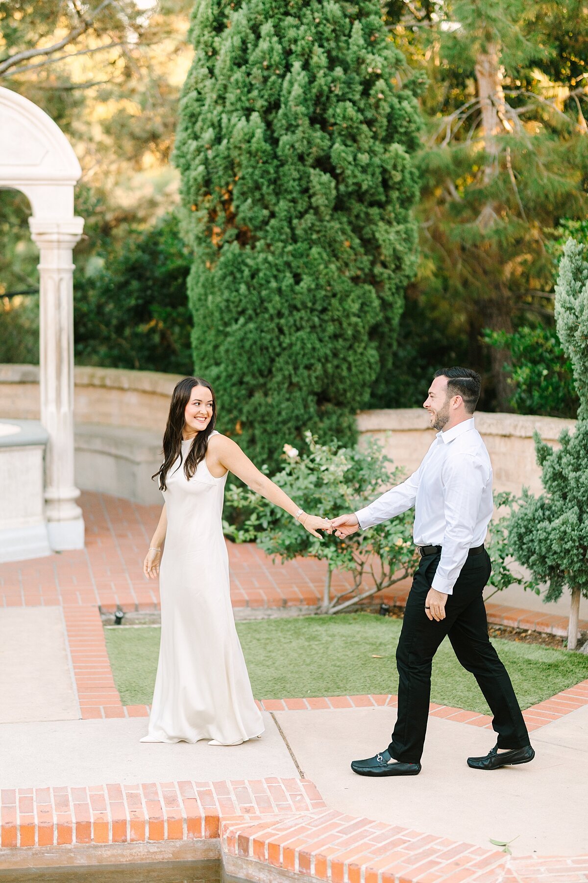 Bride leading groom walking hand in hand at Casa del rey Morro gardens in Balboa Park.
