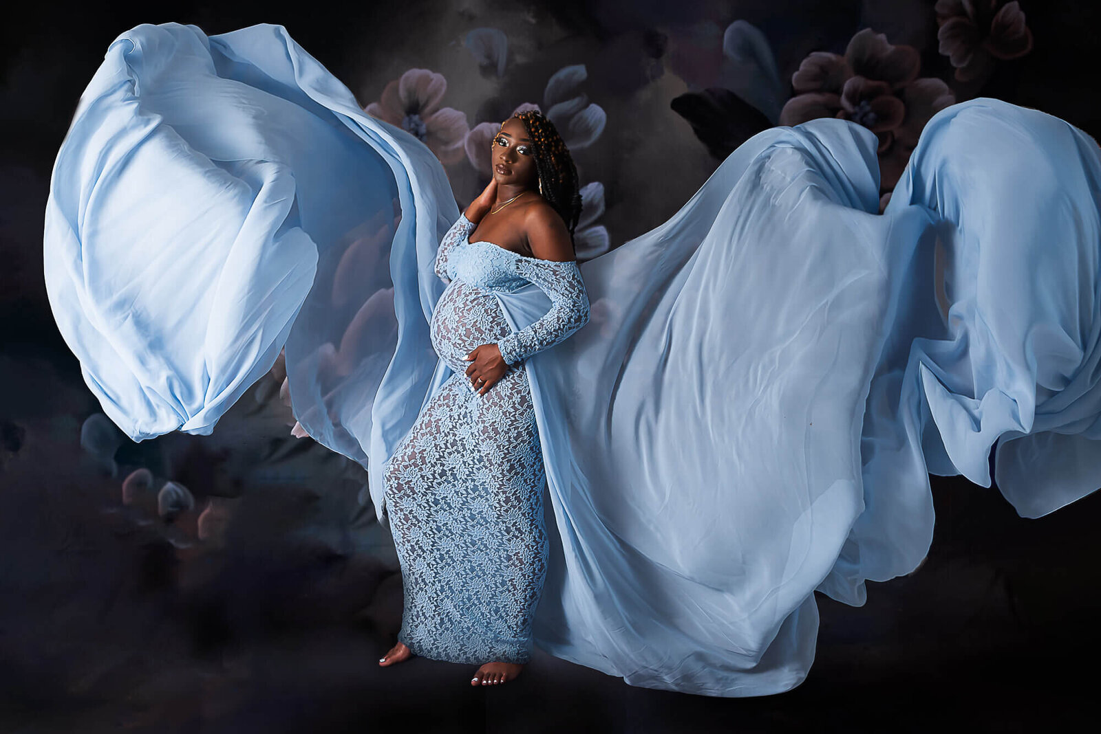 A pregnant woman in an elegant blue dress poses gracefully with her arms outstretched, exuding confidence and poise.