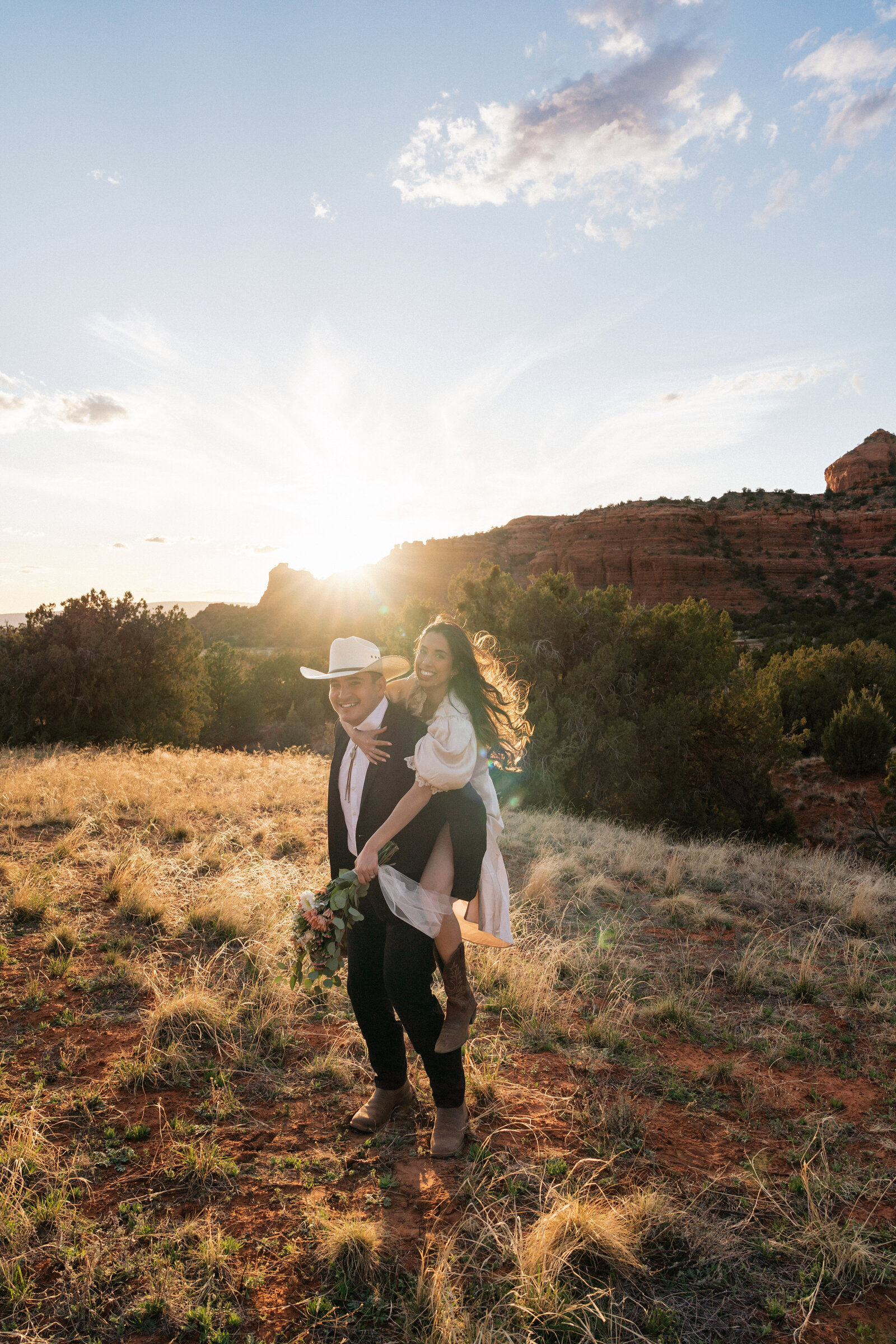 Bride laughing on groom’s back during a joyful sunset elopement at Bear Mountain in Sedona, Arizona.