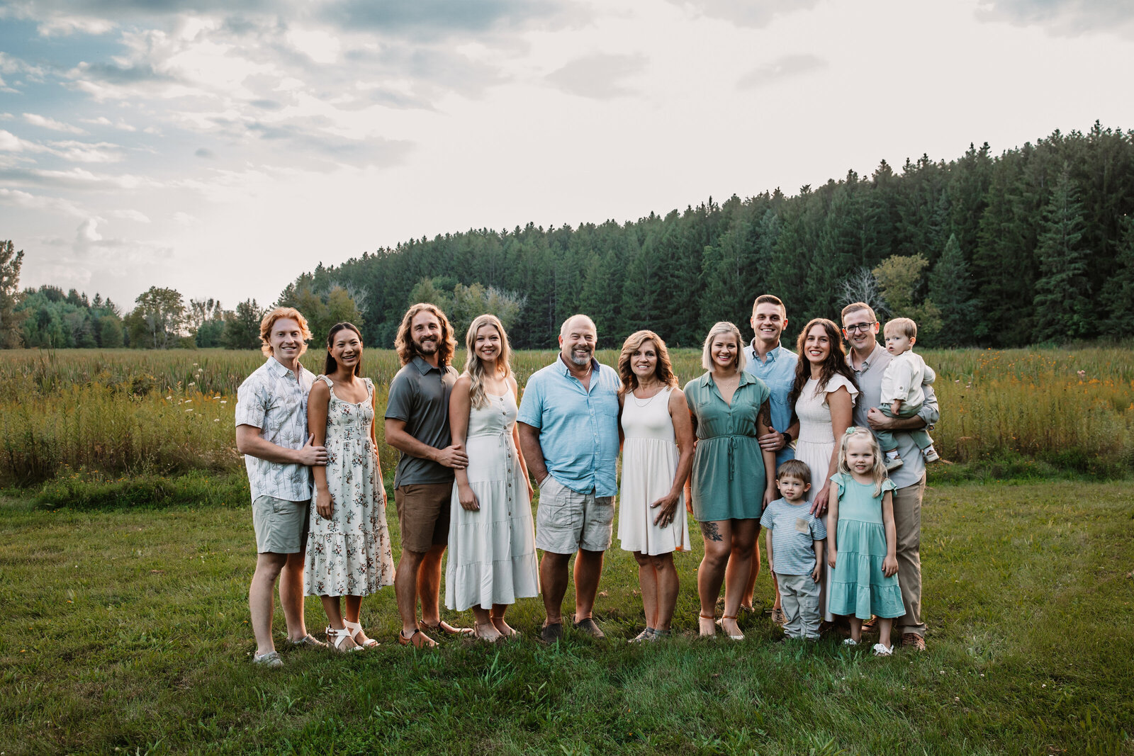 A large extended family with many children stand together in a field at sunset