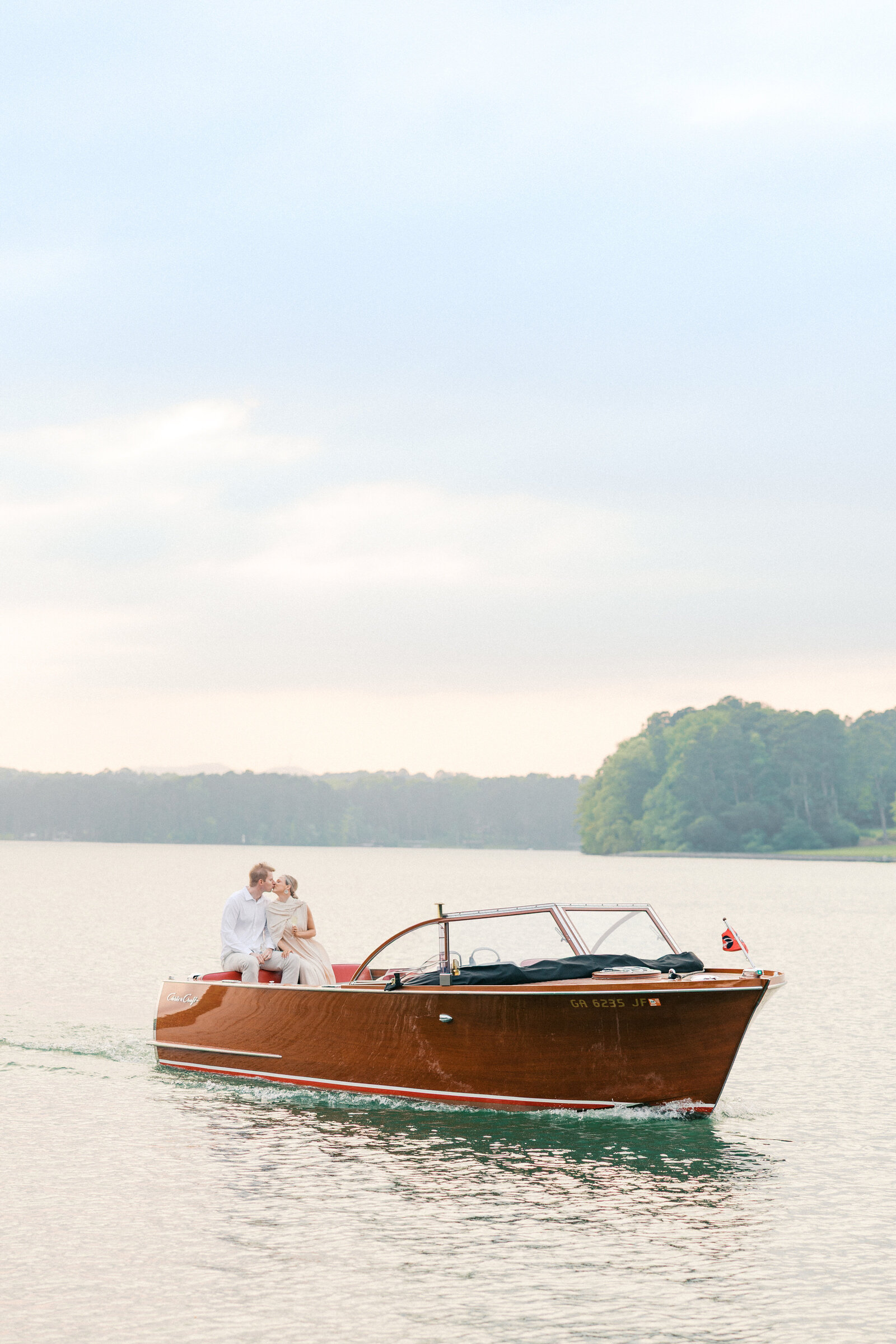 Engaged couple kisses while sitting on the back of a wooden boat engagement session on Lake Oconee