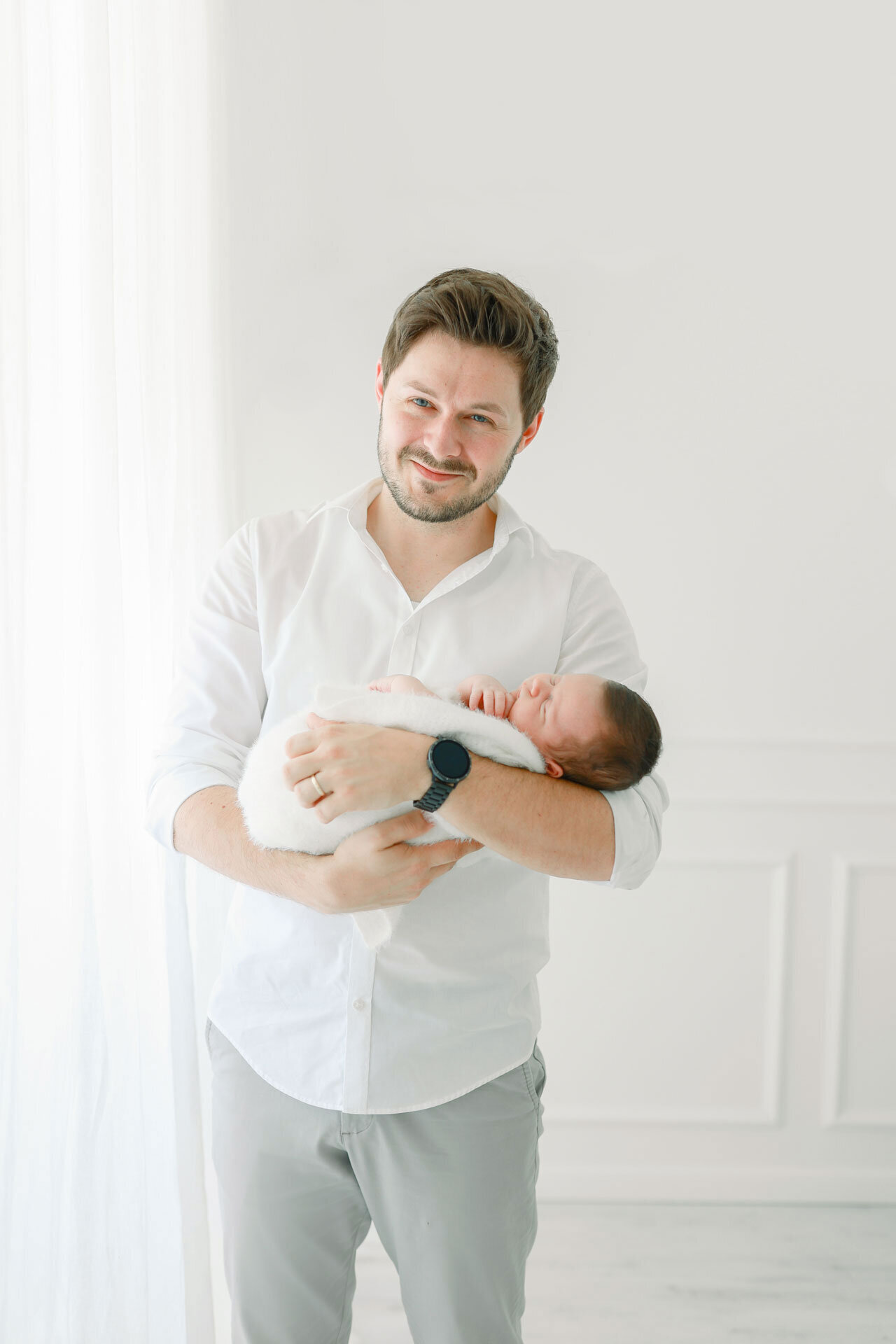 Neugeborenenshooting in Bielefeld mit Papa in einem weißen Hemd, der stolz und glücklich seinen Neugeborenen im Arm hält.