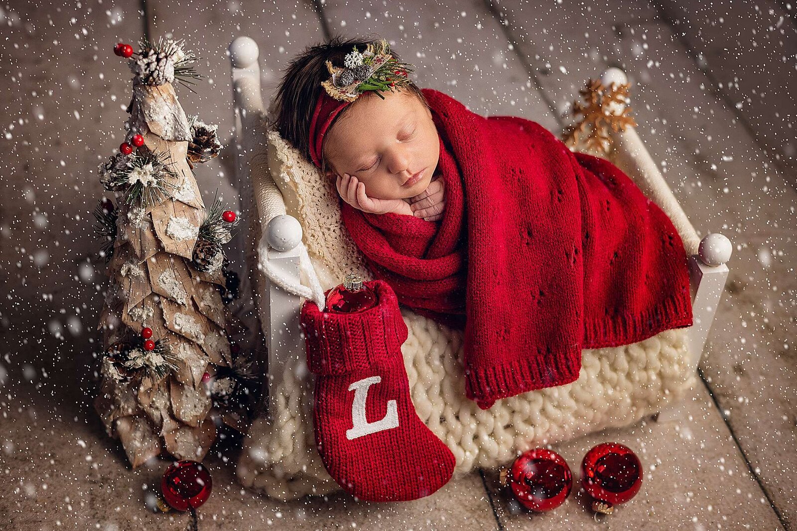 A peaceful newborn girl wrapped in a red blanket, sleeping soundly on a wooden bed, captured by Bia Schaefer Photography.