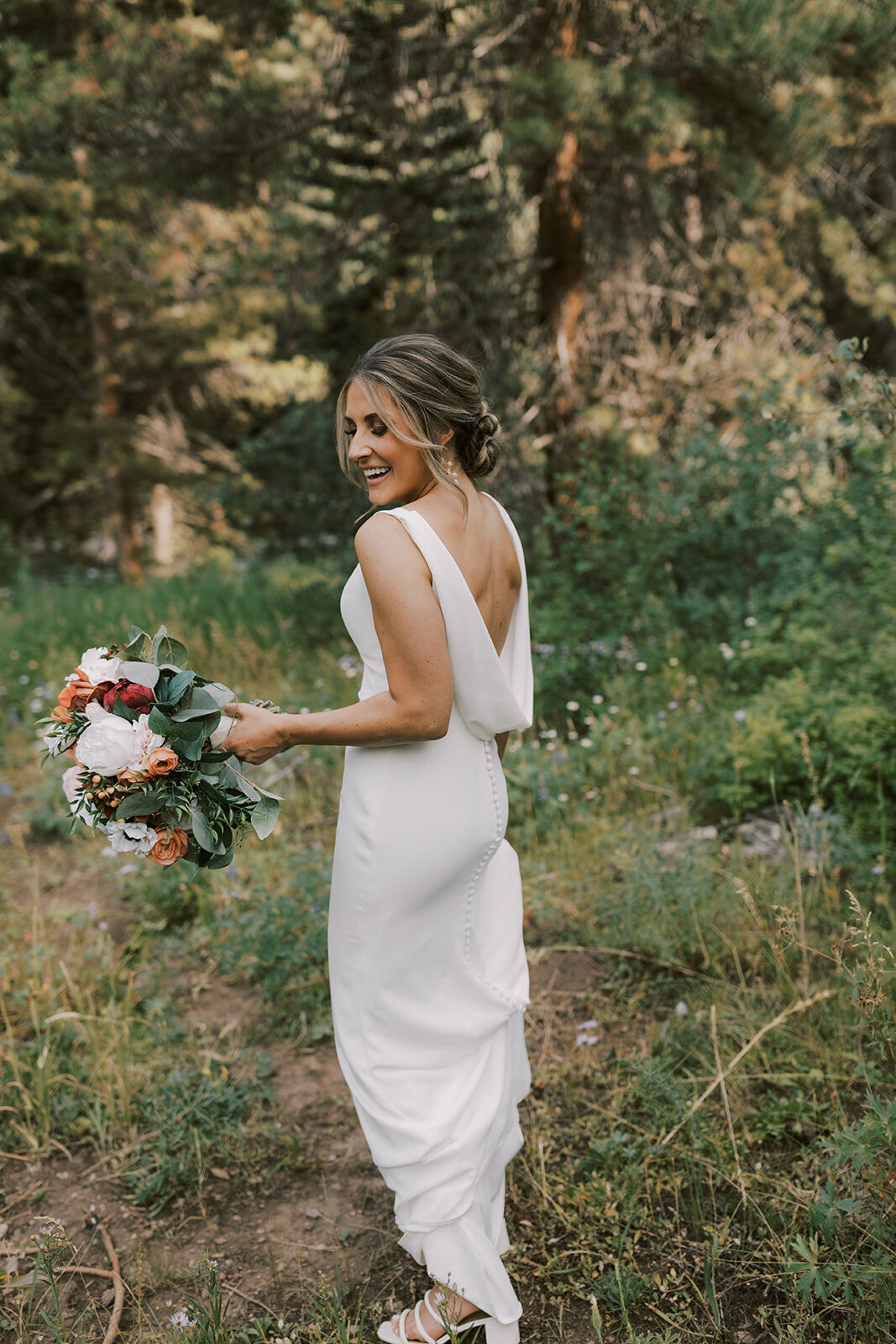 Bride in her wedding gown happily walking  through filed of grass while holding her wedding bouquet