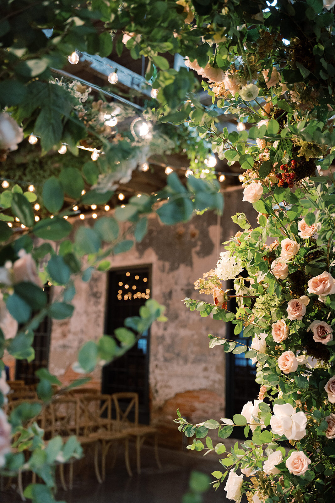 Full floral arch including white, blush, and peach garden roses and greenery hanging from the ceiling.