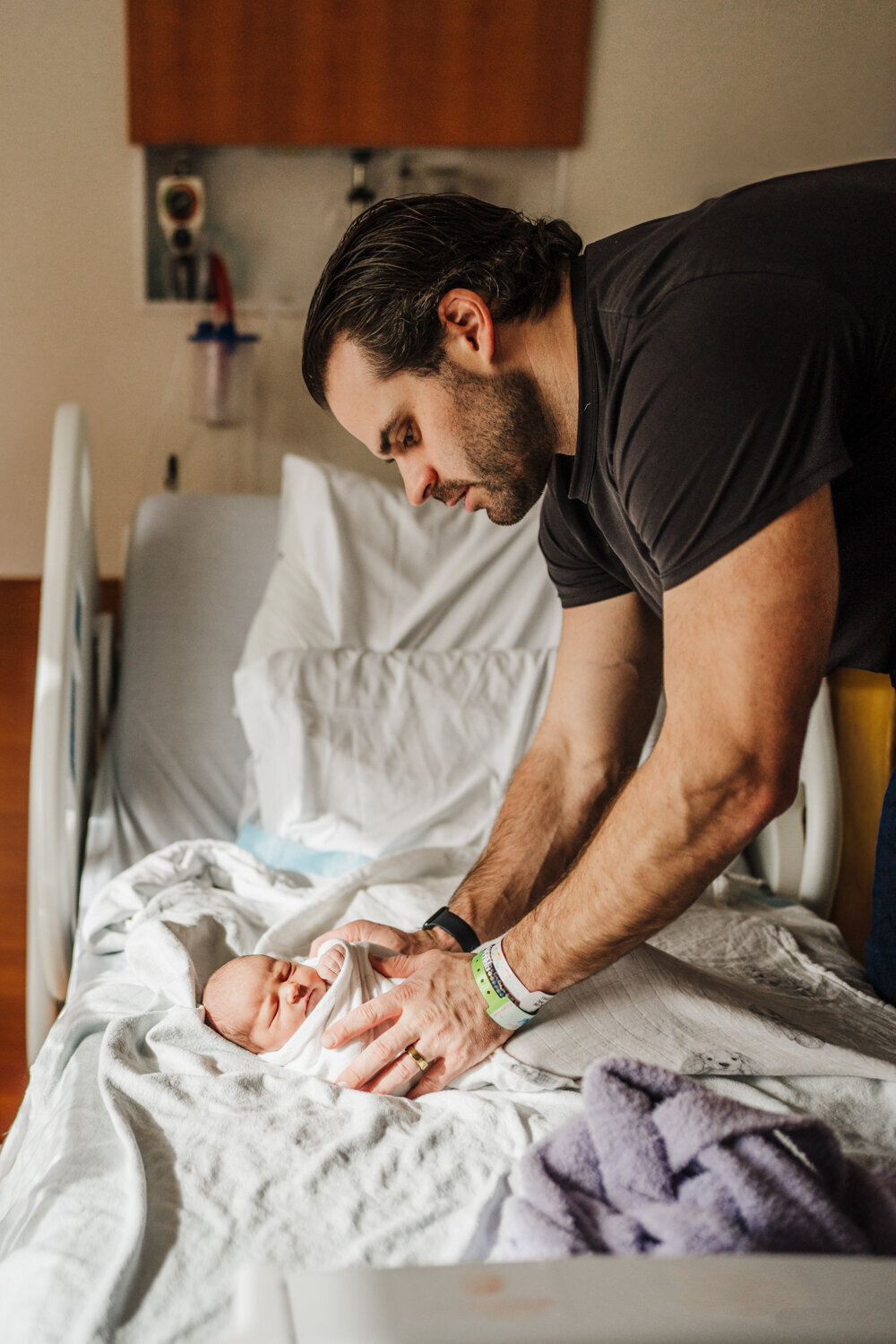 dad swaddles newborn on hospital bed