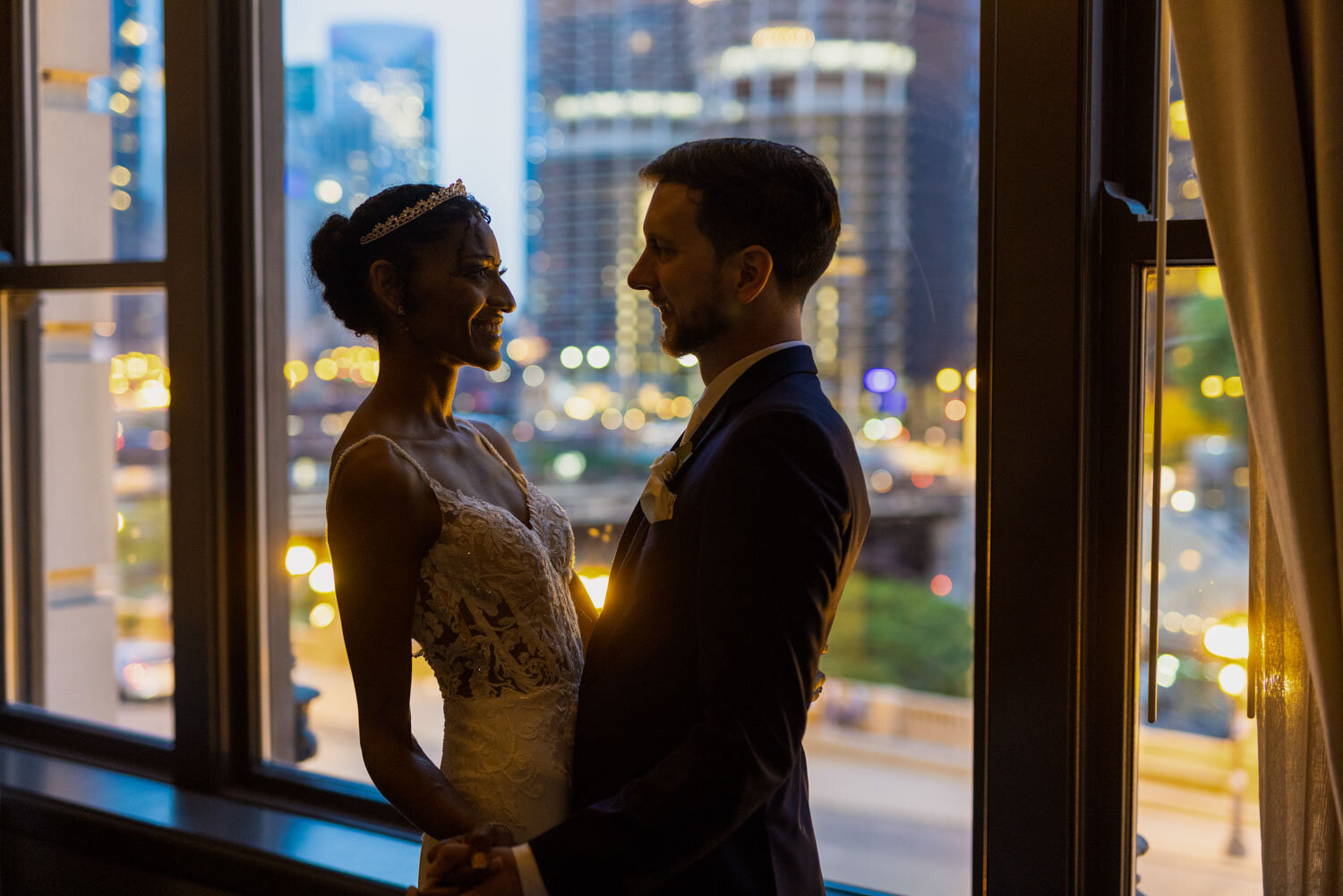 A bride and groom are looking at each other in front of a window.