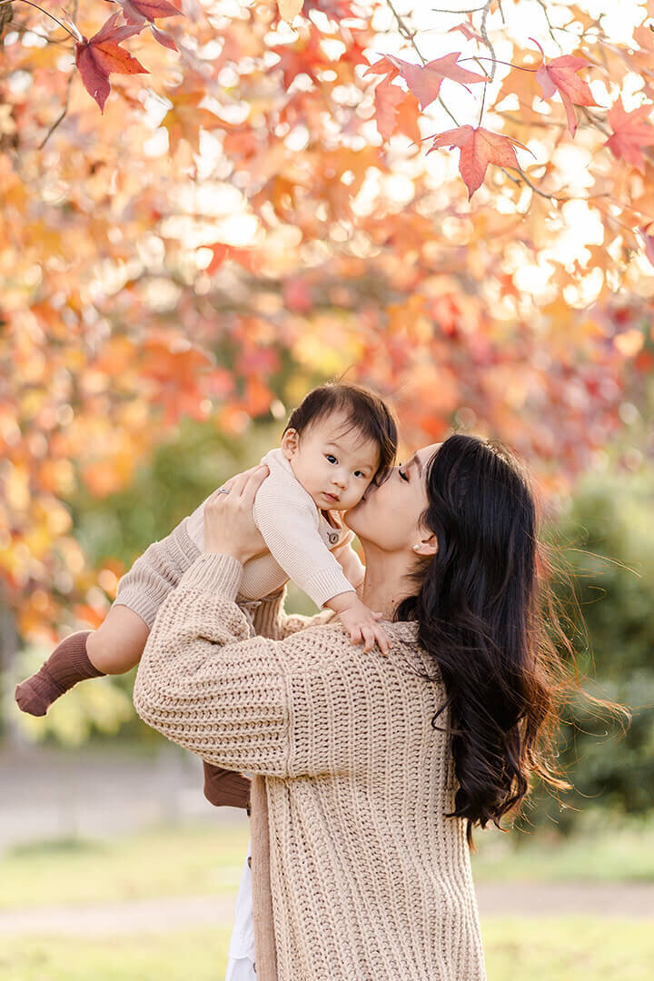mum kissing baby boy in knitwear during autumn season with gorgeous autumn colours