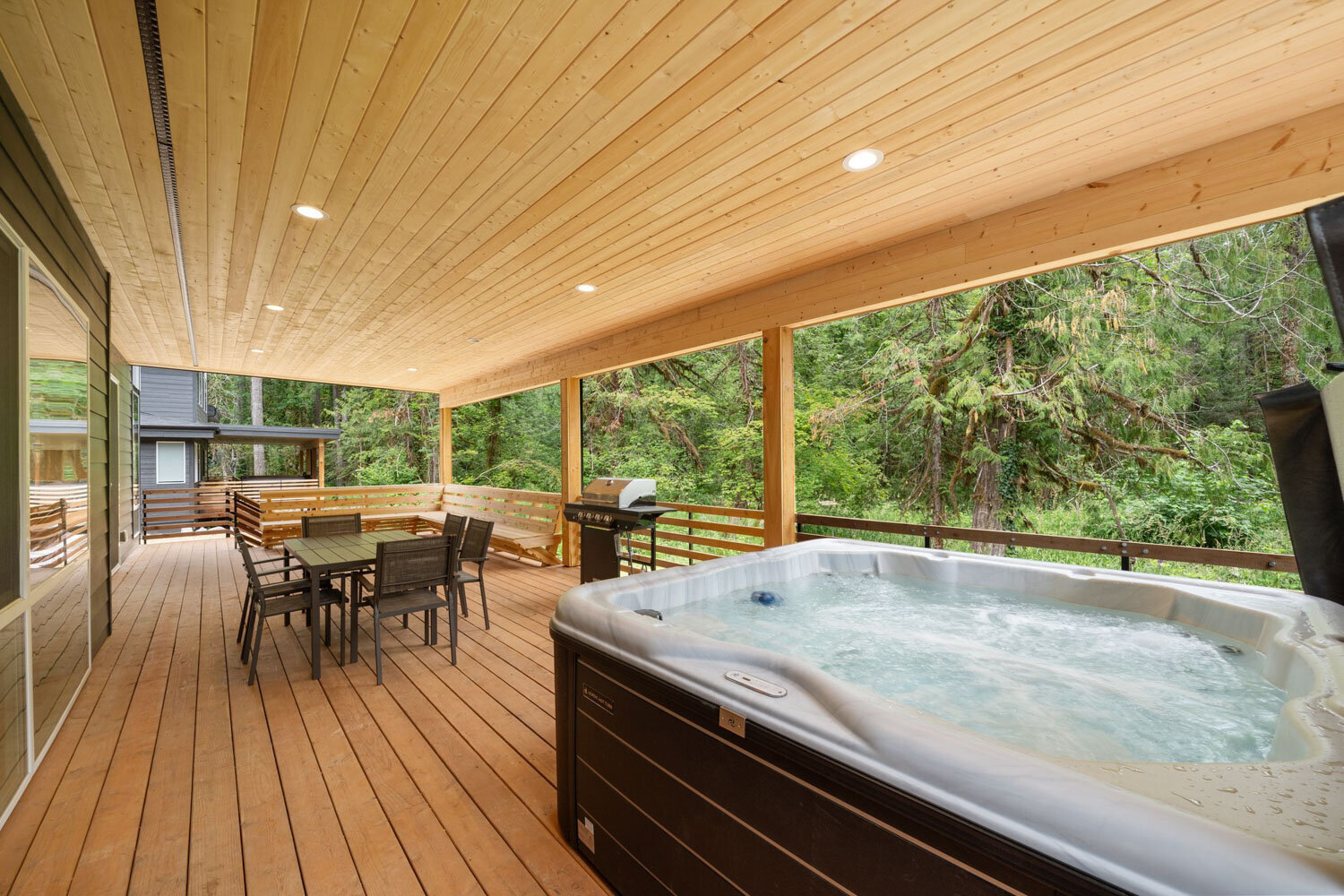 Outdoor deck with a hot tub and dining table under a wooden ceiling