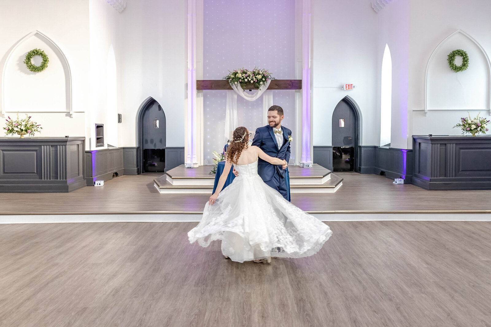 The bride and groom share their first dance in a beautifully restored historic chapel with floral decor and soft lighting, captured during a Asheville, NC wedding, showcasing elegance and timeless charm.
