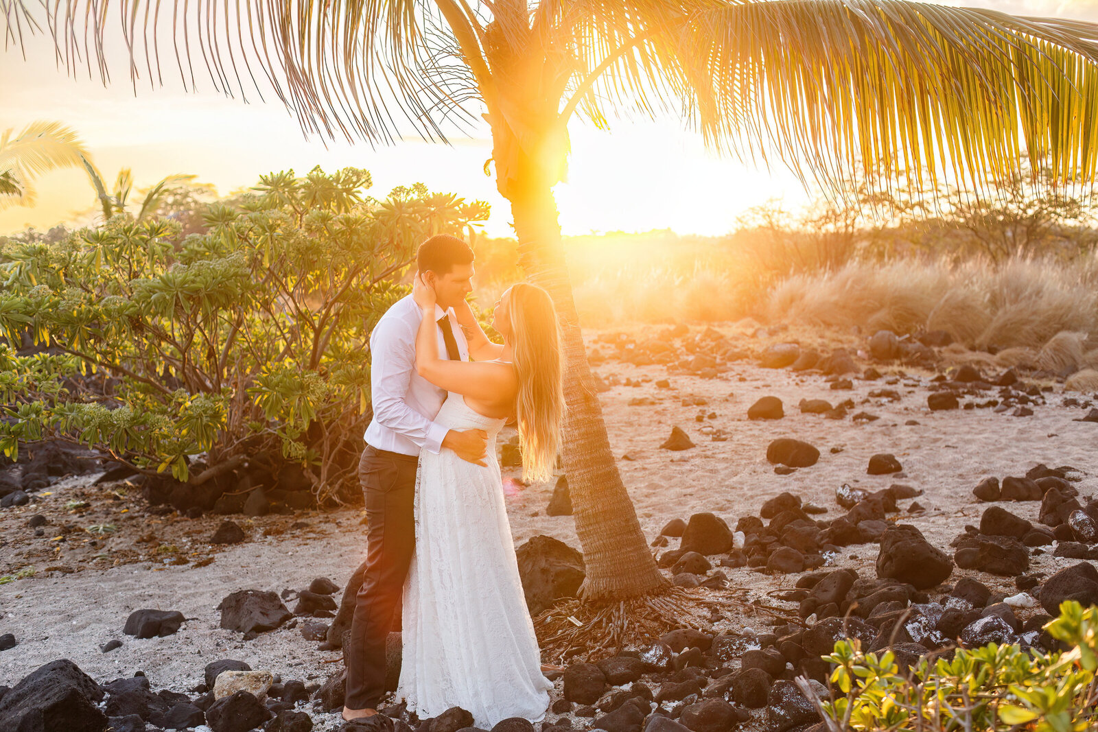 A bride and groom hugging on the beach in Hawaii at sunset.
