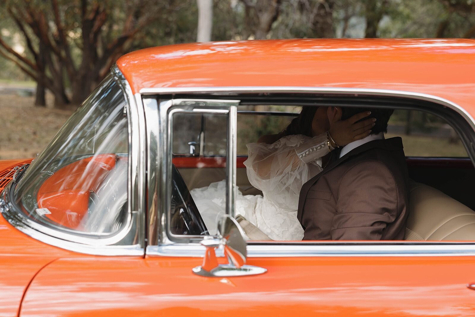 Bride and groom kissing inside a vintage orange getaway car