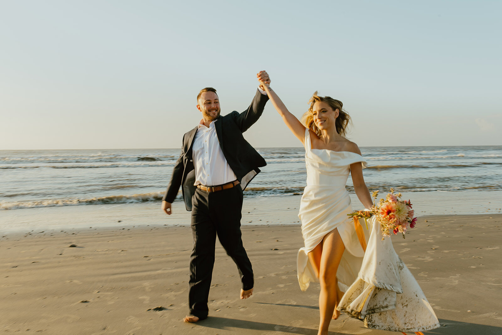 bride and groom run hand in hand on beach