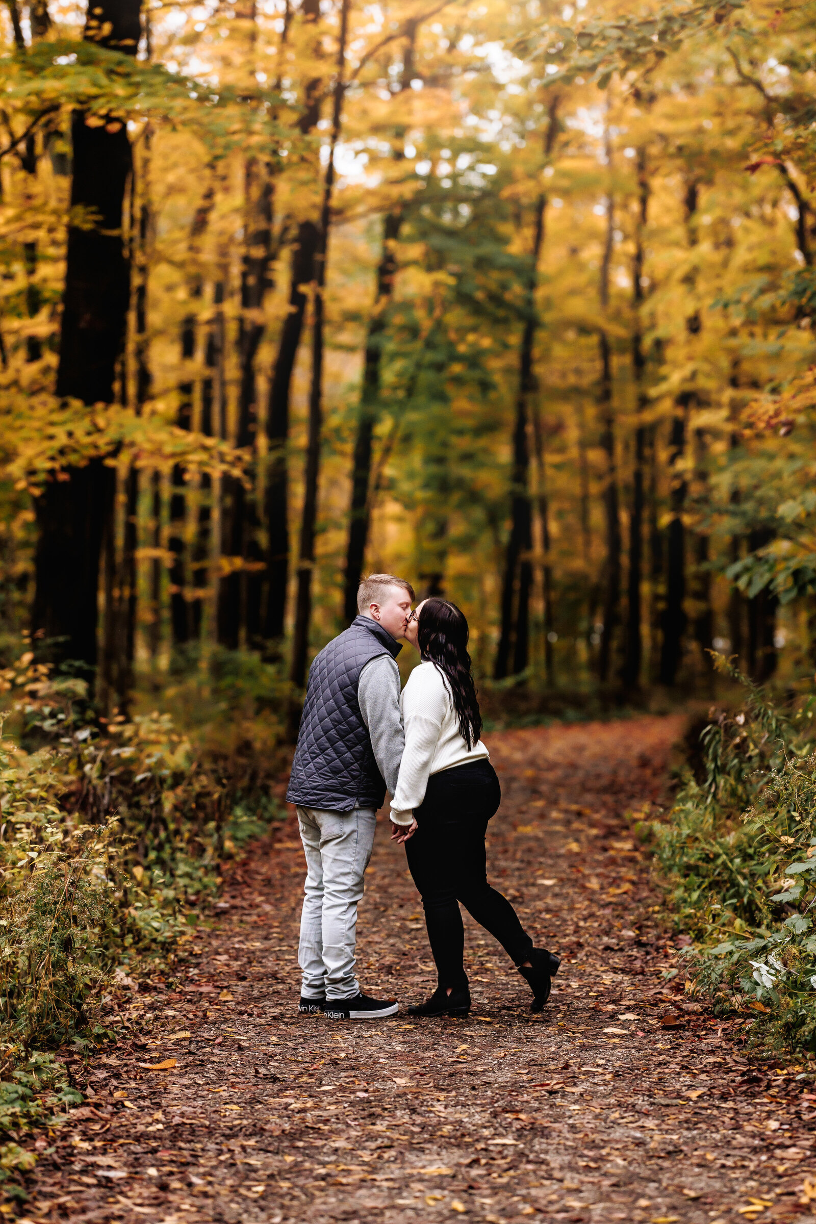 Couple stops for a kiss along a path lined with beautiful fall foliage