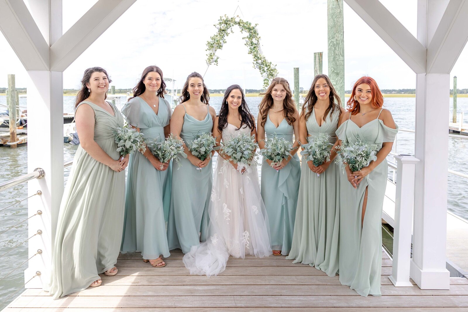 Bride surrounded by her bridesmaids in elegant mint green dresses, captured at a waterfront venue in Wrightsville Beach, NC. 