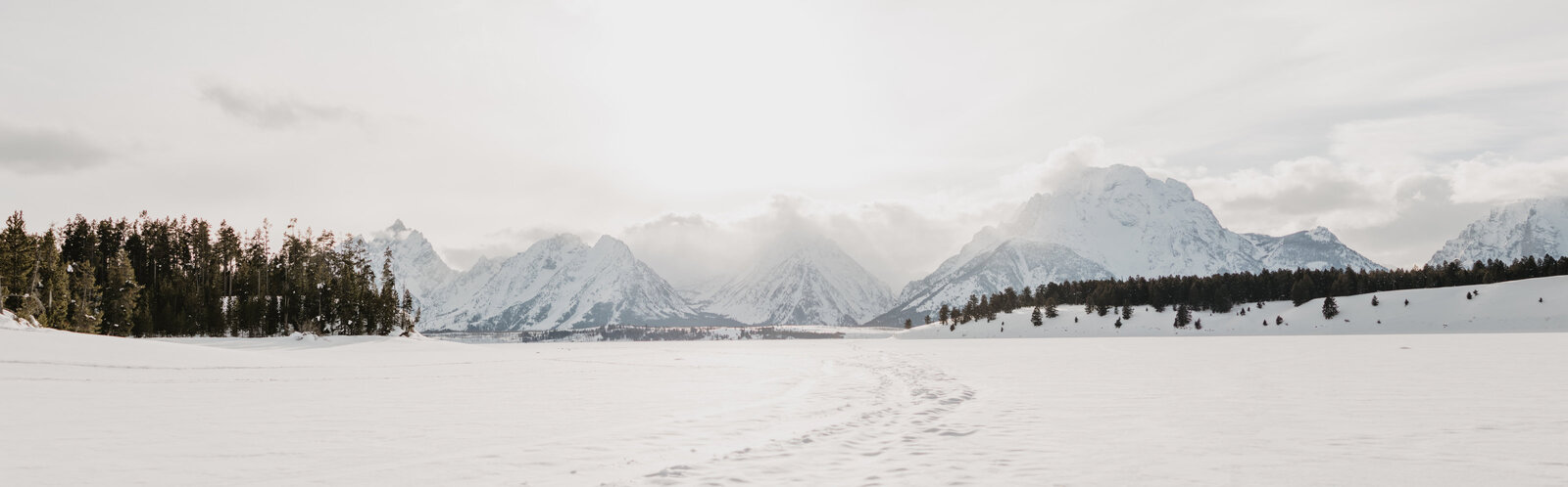 Jackson Lake in the Grand Tetons during the winter with the lake frozen over with the mountains  through the fog in the distance captured by jackson hole photographers