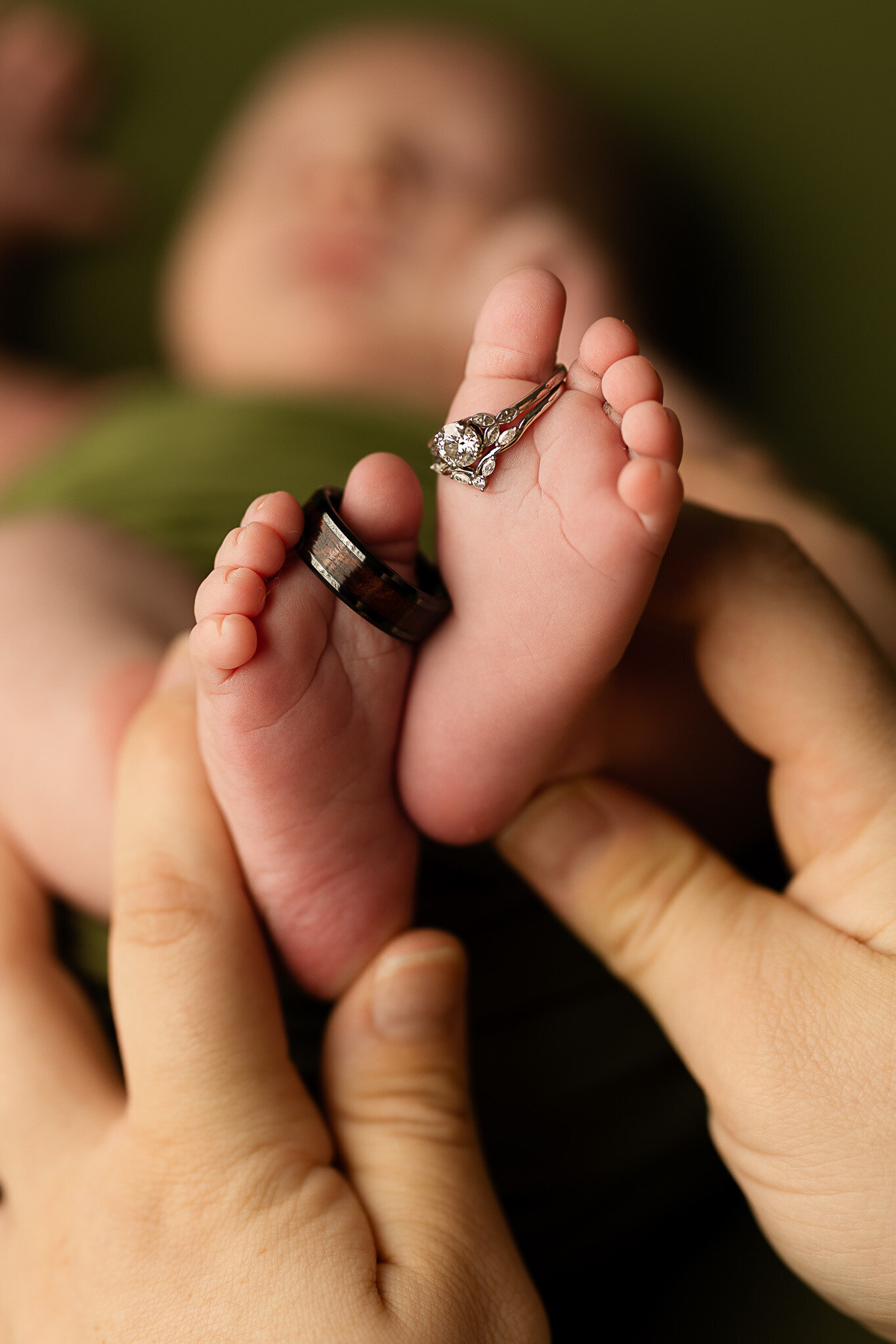 Close up of newborn feet with his parents wedding rings daintily placed on his toes.